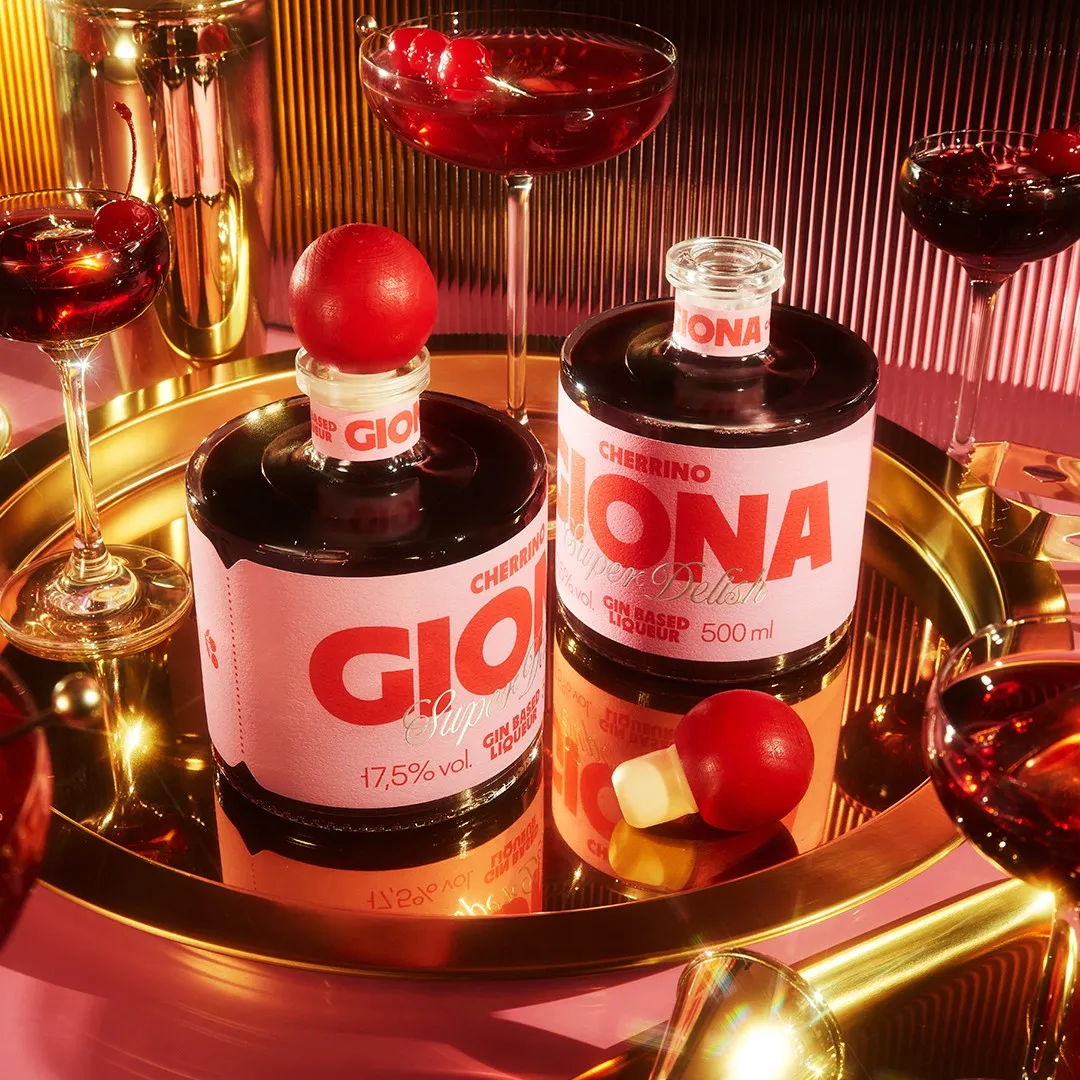 Two Giona Cherrino liqueur bottles with pink labels on a gold tray with cherry cocktails, bottle design