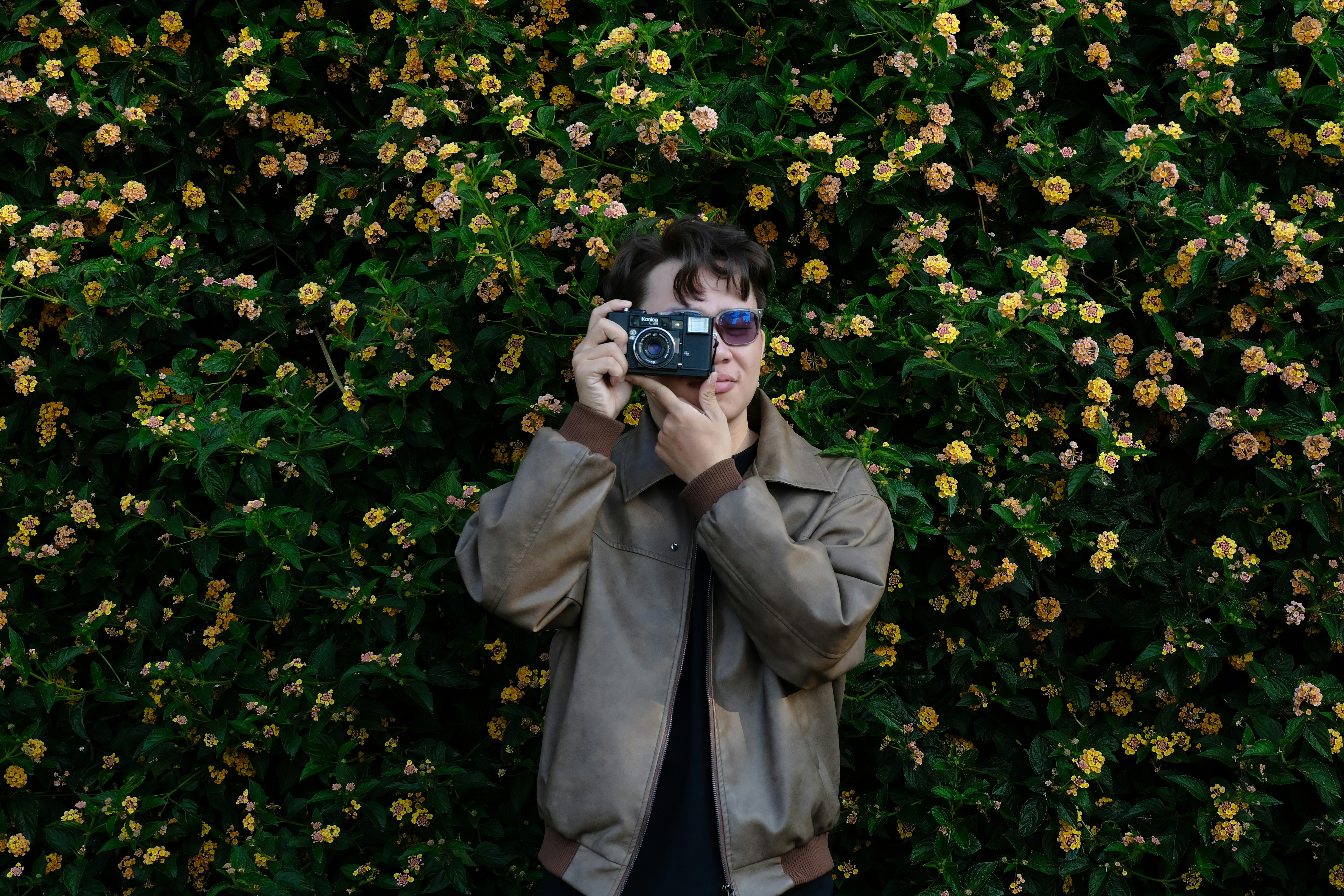 Person holding vintage camera in front of blooming flowers
