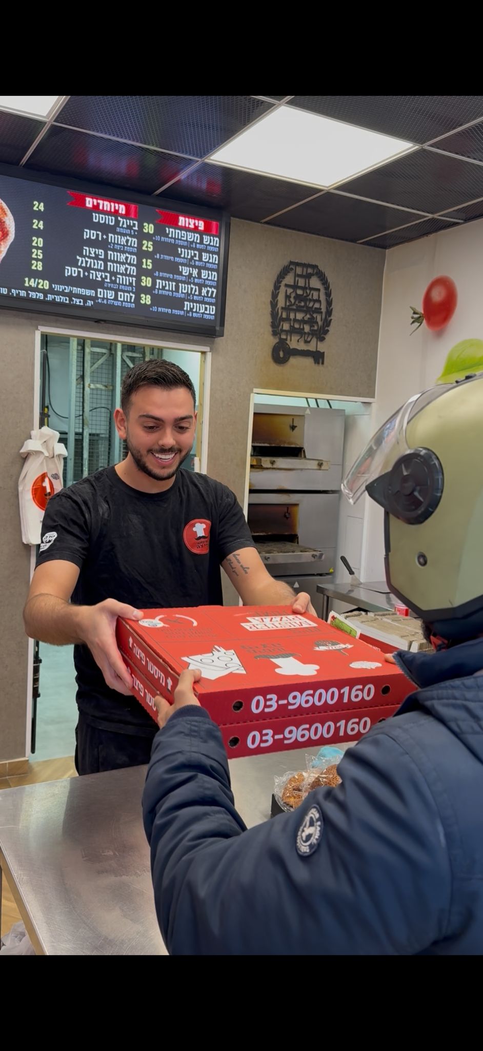 שליח מקבל קופסאות פיצה בדלפק פיצרייה.