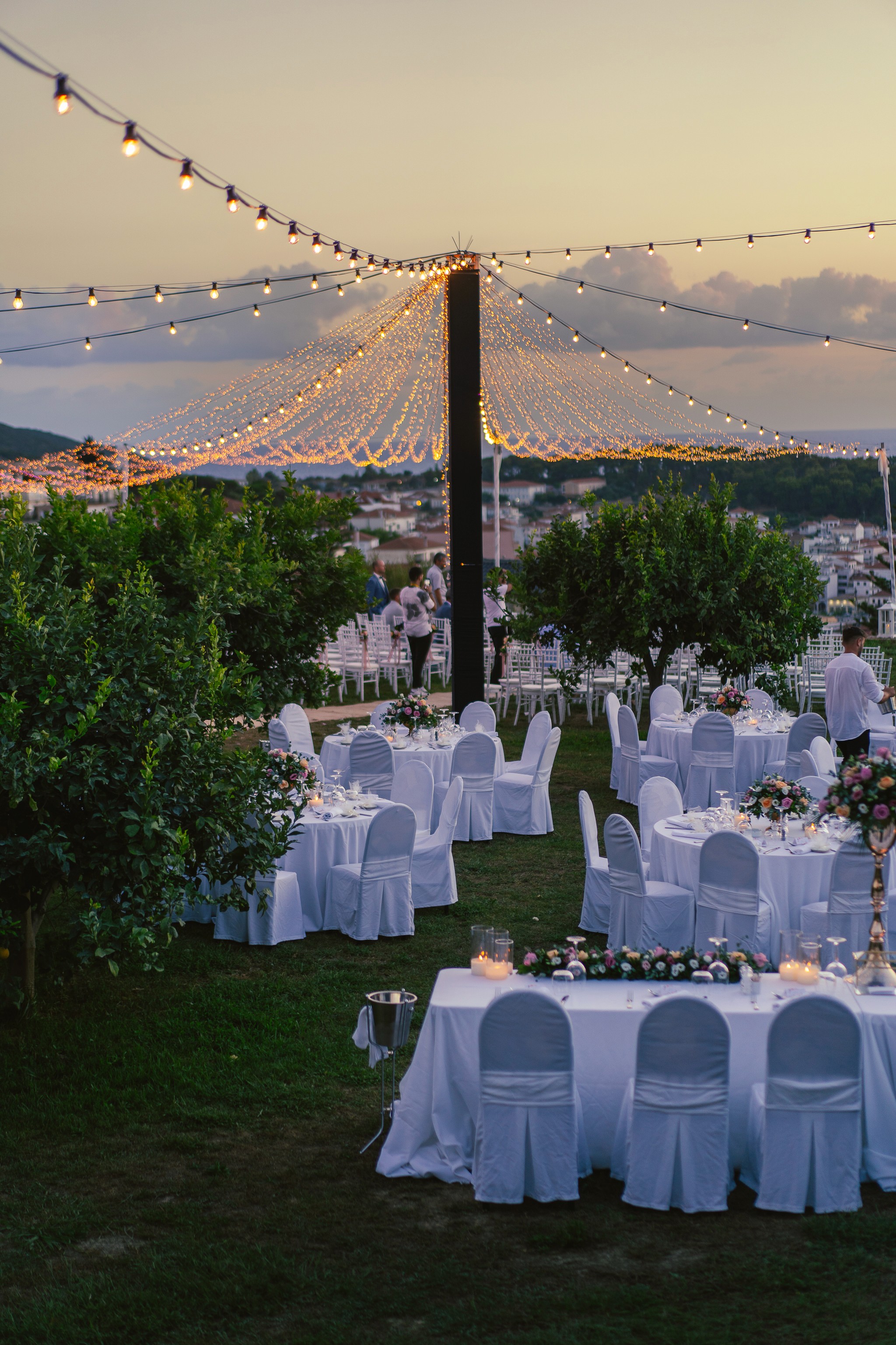 Υπαίθρια δεξίωση γάμου στο ηλιοβασίλεμα με λαμπάκια και στρογγυλά τραπέζια στην Πελοπόννησο