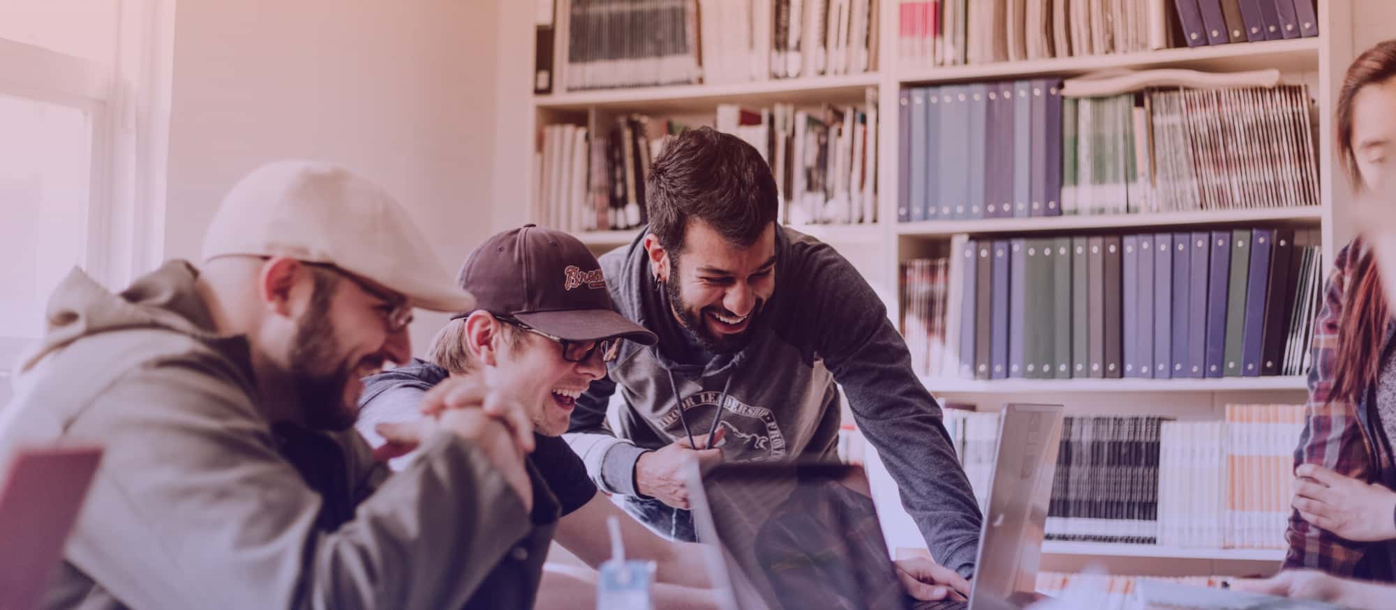 Four colleagues laughing and discussing around a laptop during an office meeting.