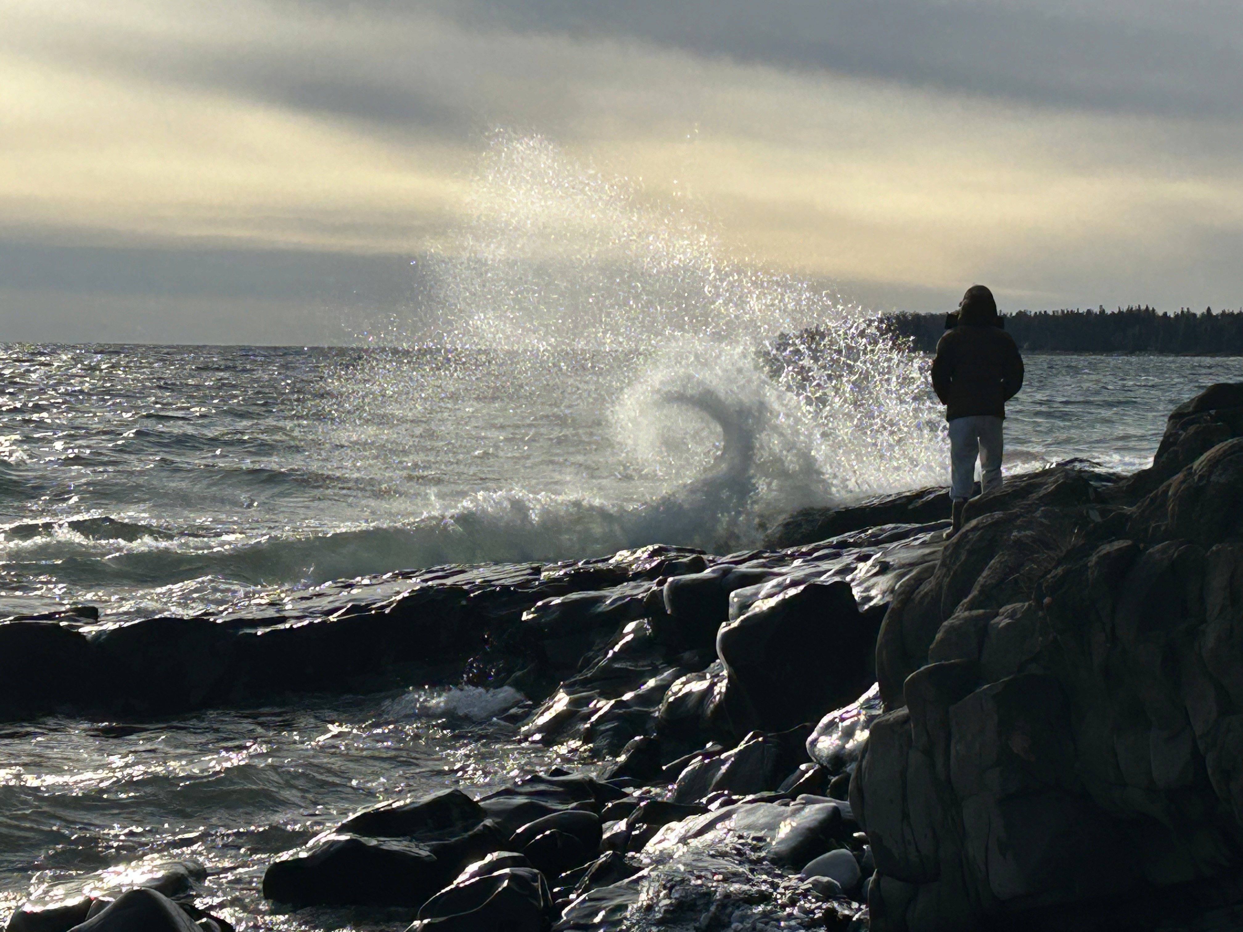 A person standing on rocks as ocean waves crash along the shoreline.