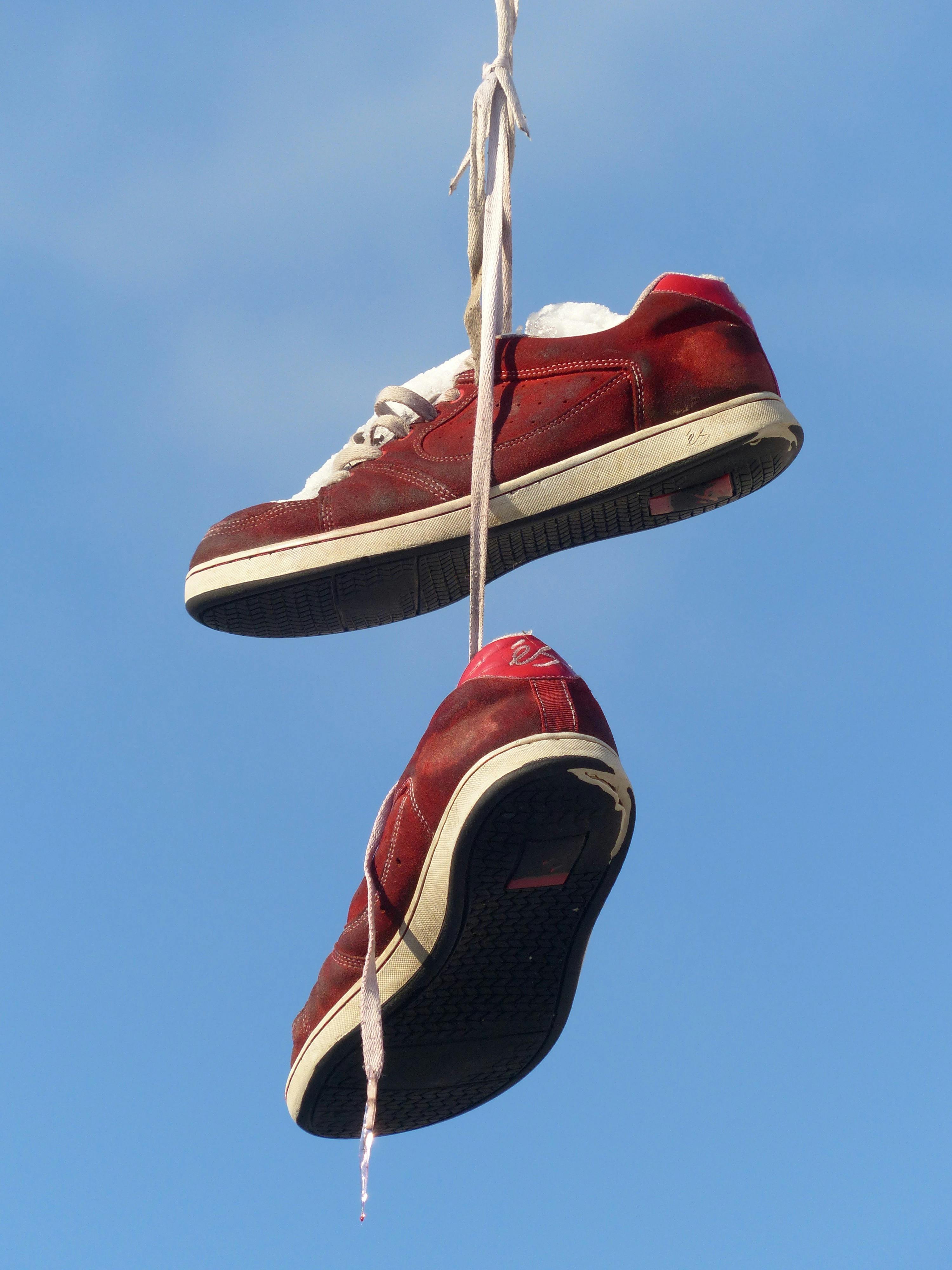 A pair of red sneakers hanging by their laces against a blue sky