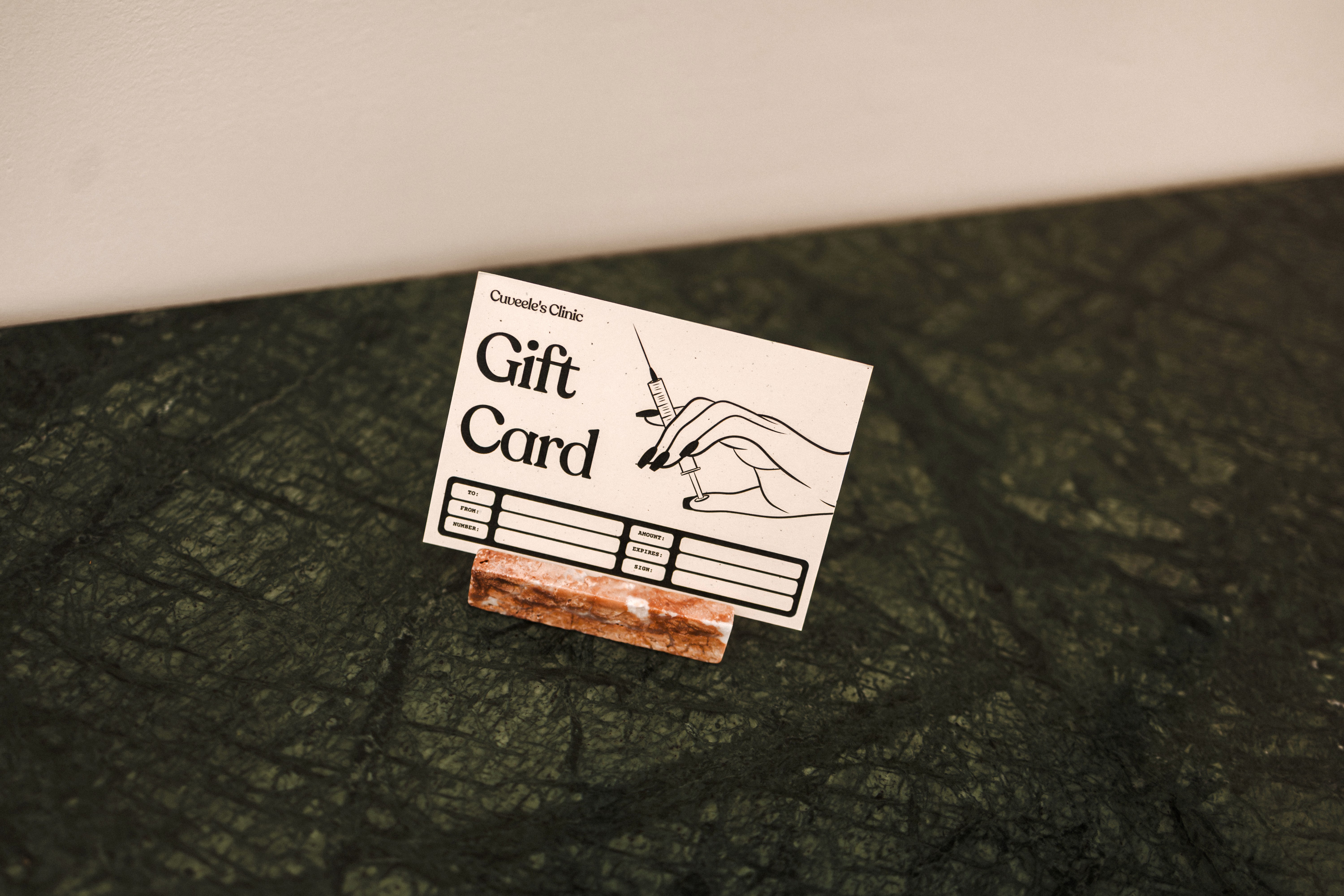 A Cuveele's Clinic gift card presented on a green marble surface.