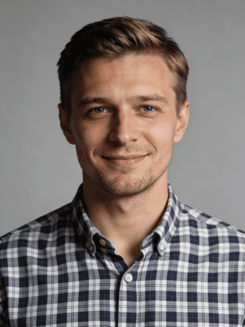 Portrait of a smiling man in a plaid button-up shirt against a gray background.