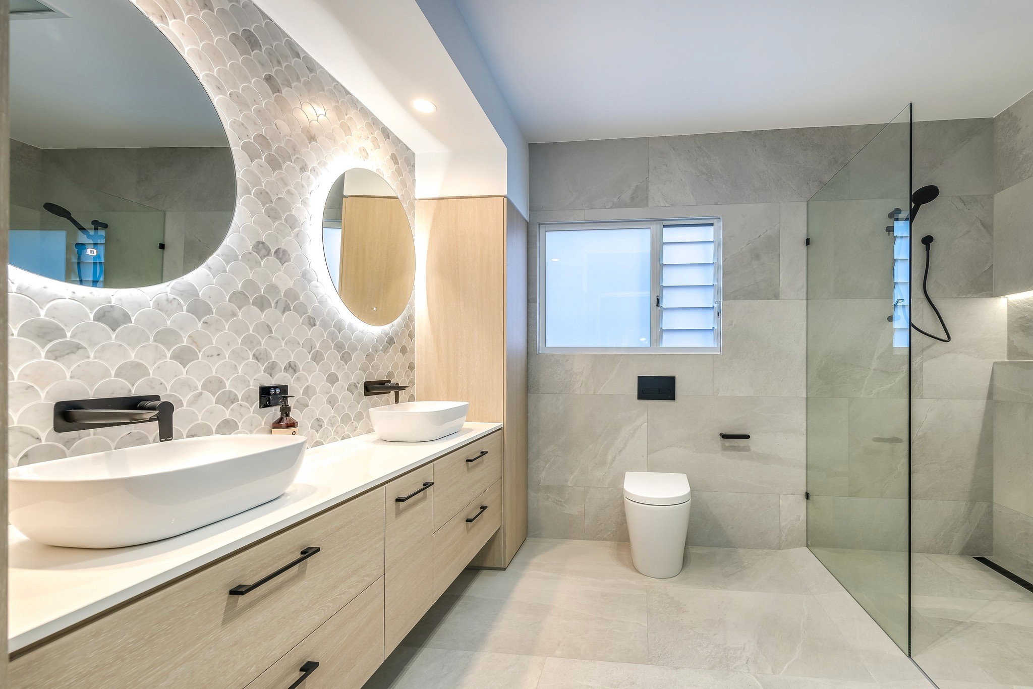 Bathroom renovation Eumundi design reference: Double timber vanity, round mirrors and frameless shower in a grey tiled bathroom