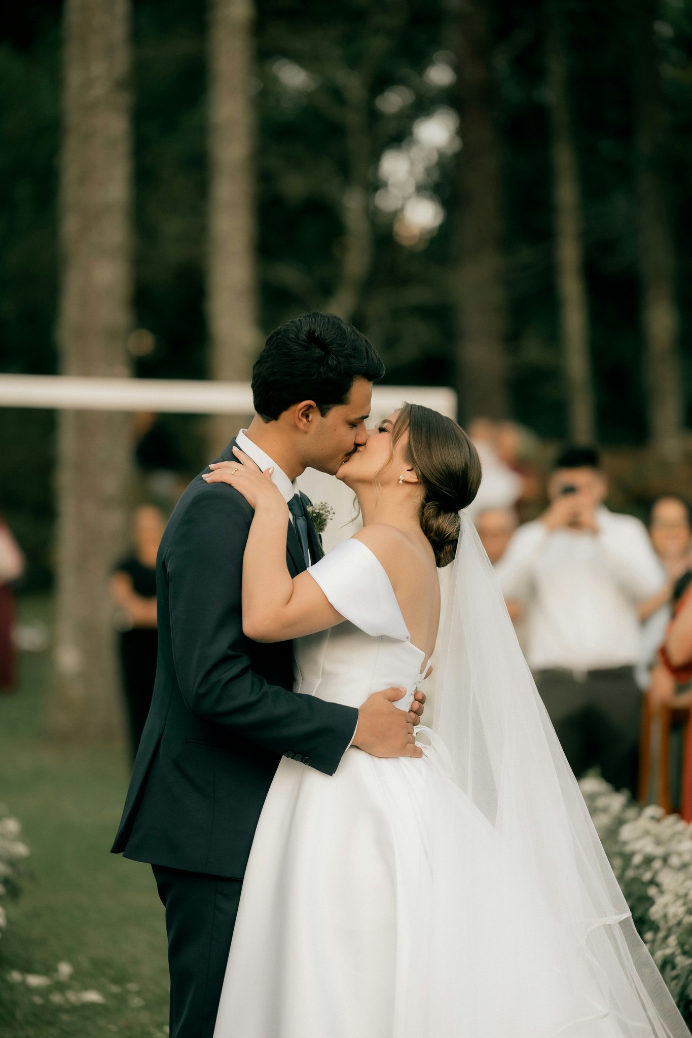 Newlyweds kissing as the bride's veil flows behind her during an intimate woodland wedding ceremony