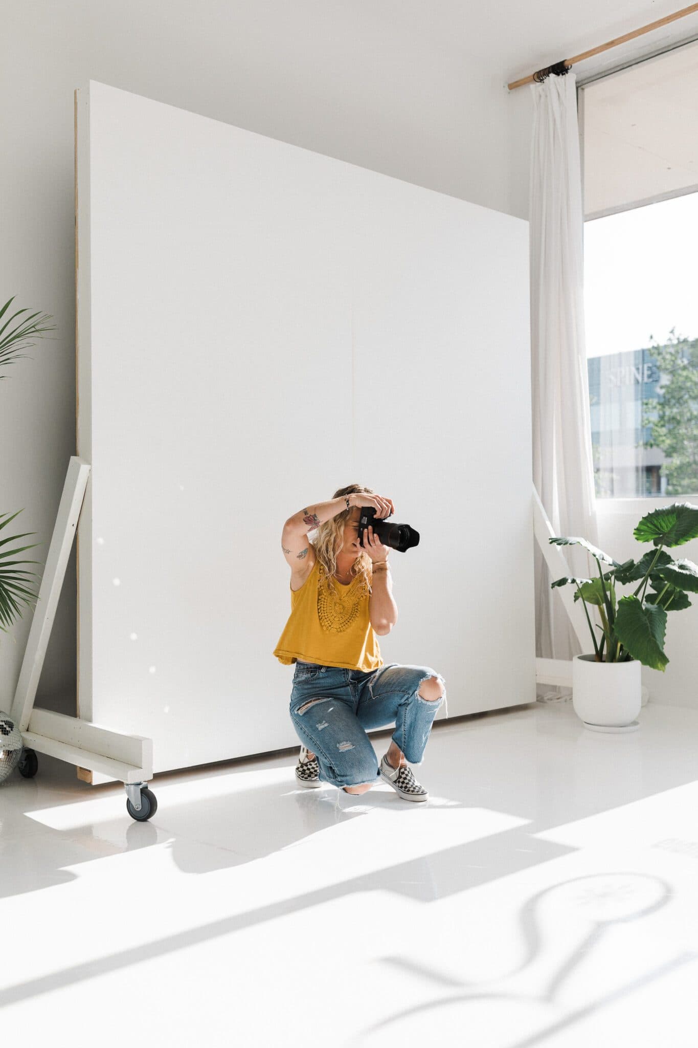 A photographer kneels while capturing a shot in the bright, natural light of Revelator Studio in Shreveport, showcasing the studio’s ideal environment for professional photography sessions.