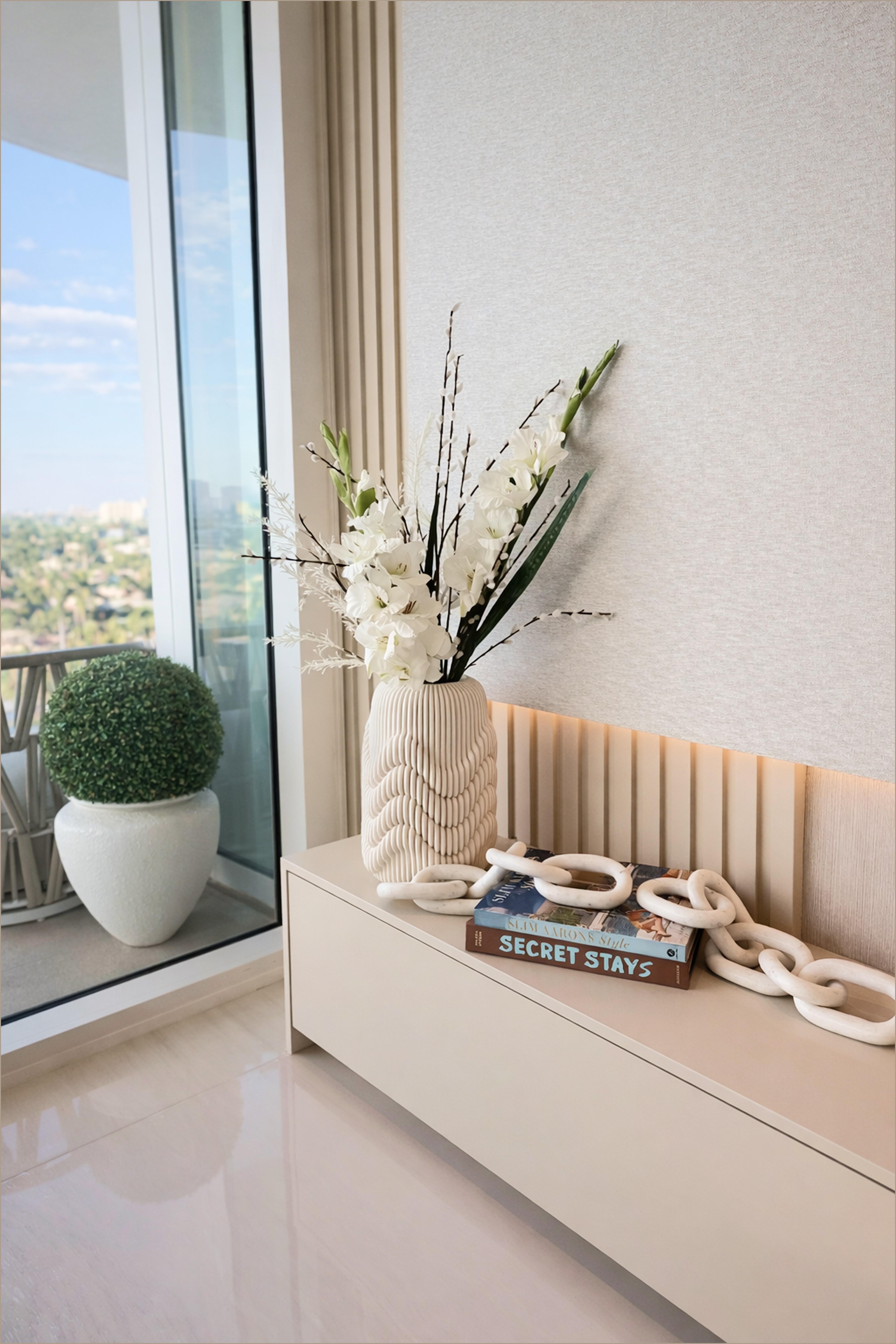 Styled luxury console with a sculptural vase, floral arrangement, and soft natural light by the window.