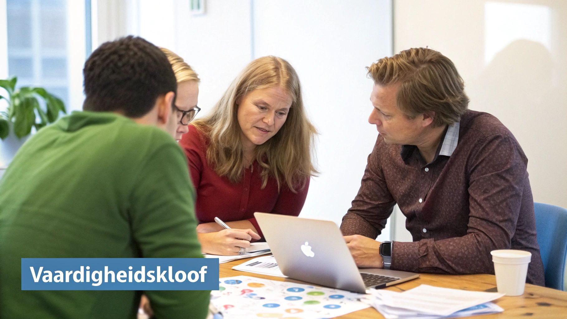 Vier mensen zitten rond een tafel en bespreken de 'vaardigheidskloof' met een laptop en documenten.