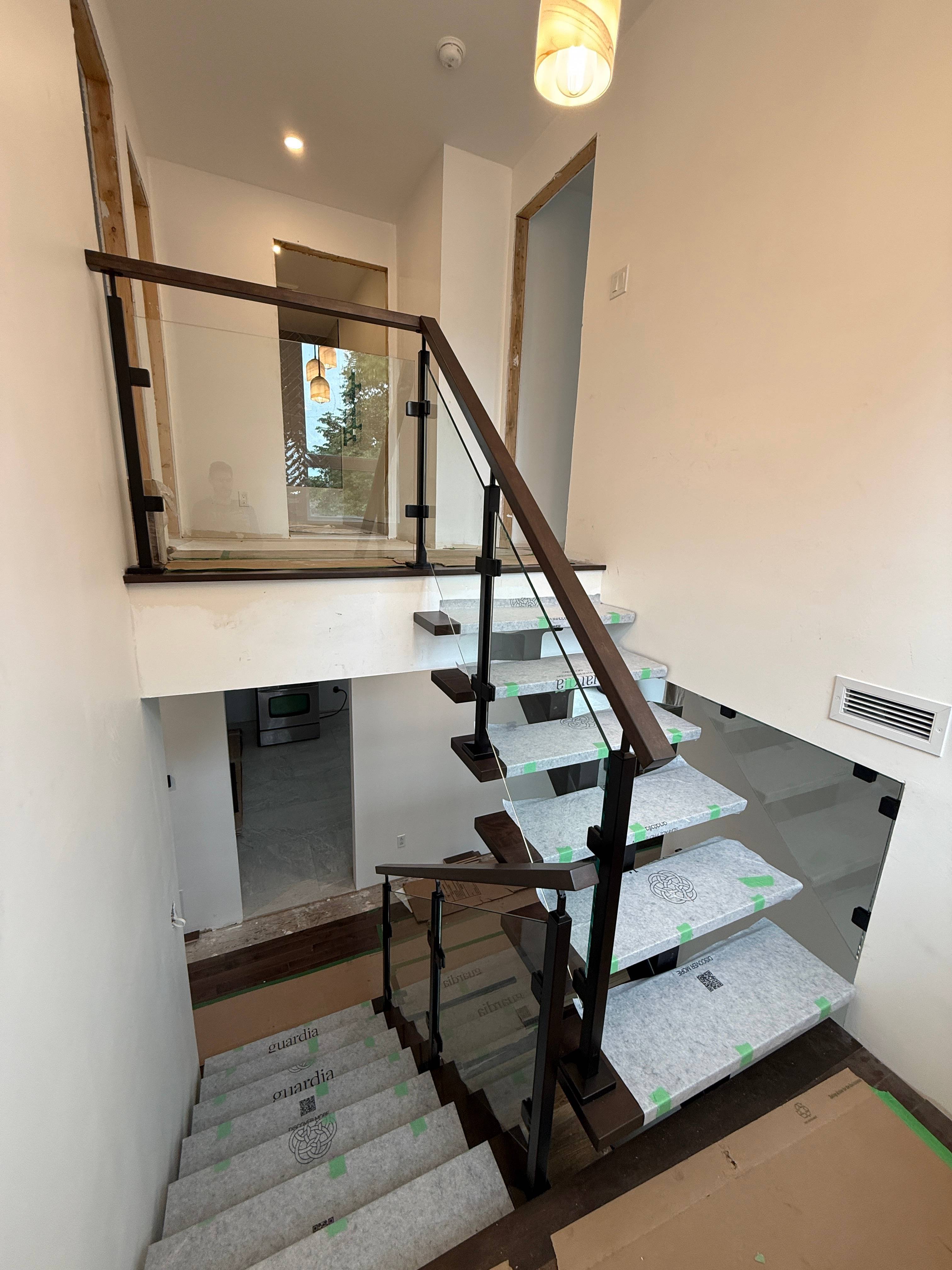 Escalier à limon central noir avec marche de départ triangulaire et garde-corps vertical, dans un projet de rénovation