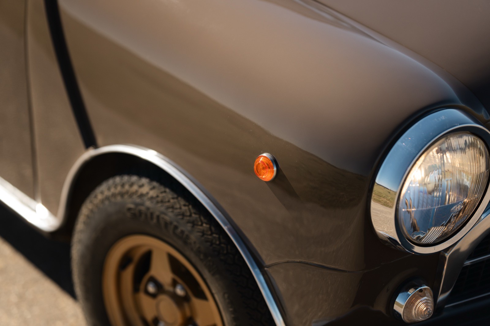 Close-up of a brown car, showcasing the wheel, fender, and part of the headlight with a small emblem.