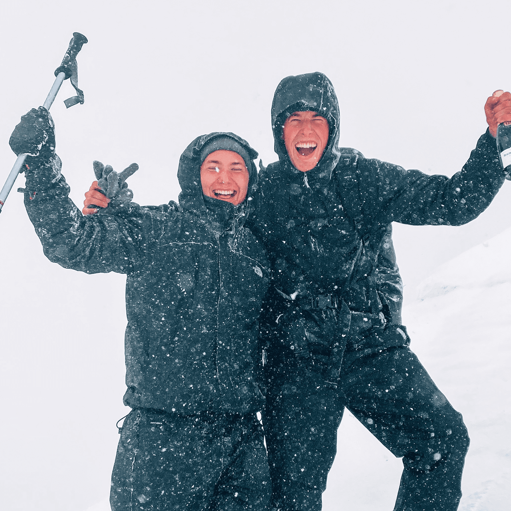 Lukas with his friend on top of a snowy mountain, holding a champange bottle