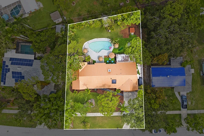 Aerial view of a Palma Sola Park area home in Bradenton with a heated pool, spacious backyard and tropical landscaping