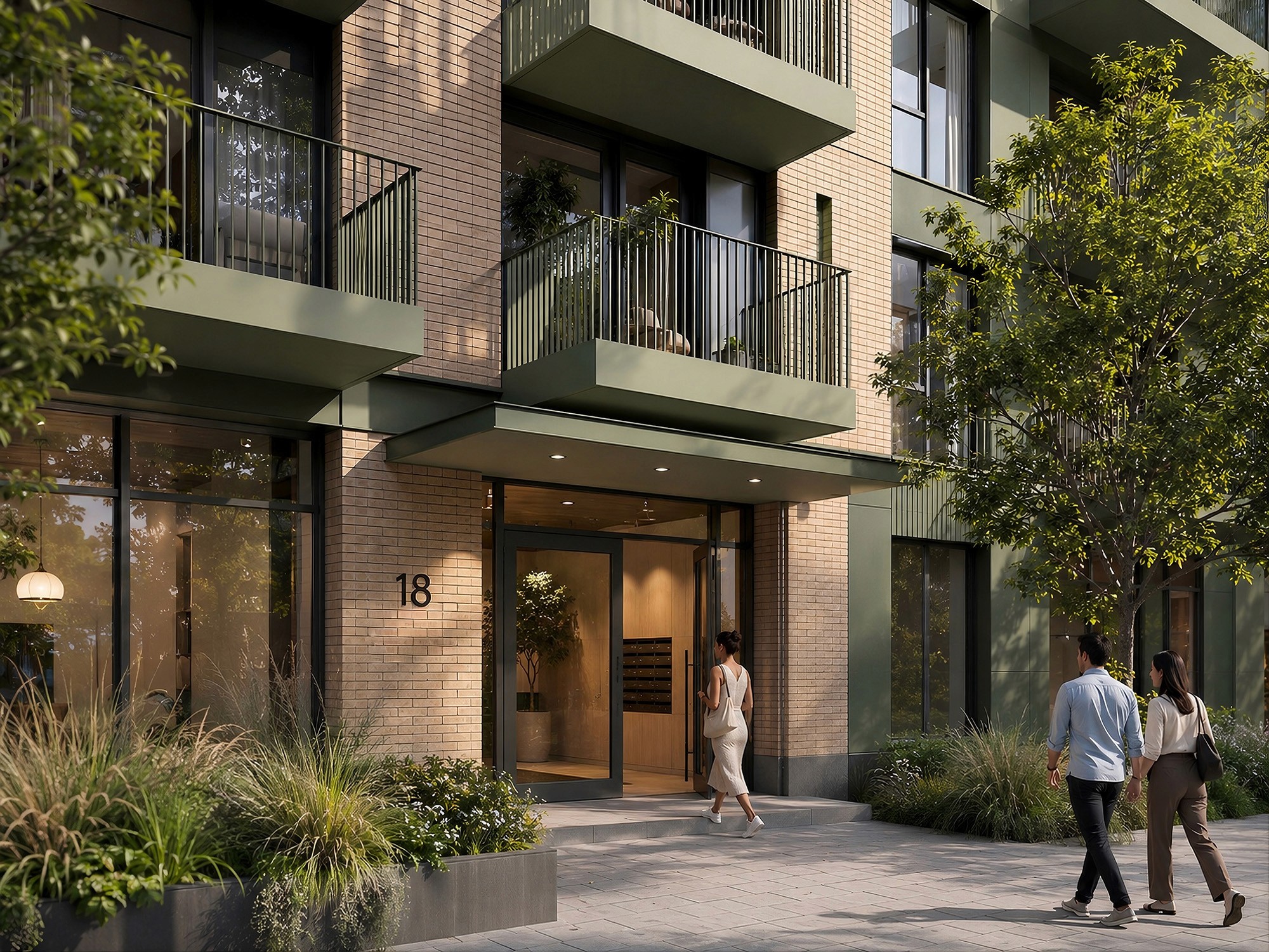 The modern glass entrance of a brick apartment building, labeled number 18, with green balconies above.