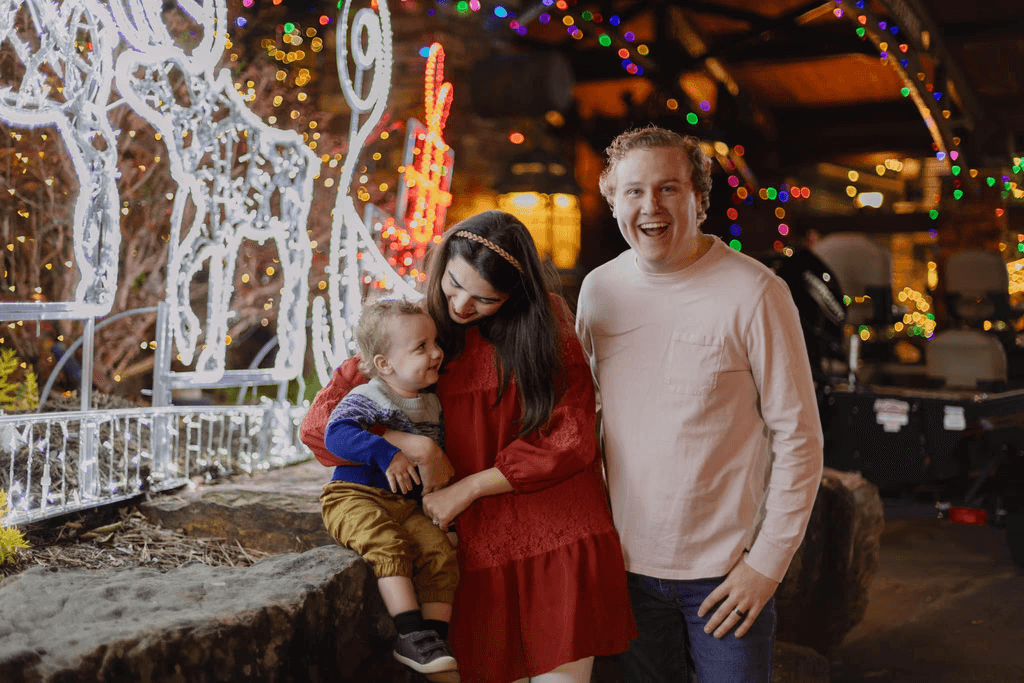 photo of young parents with their toddler and christmas lights in the background