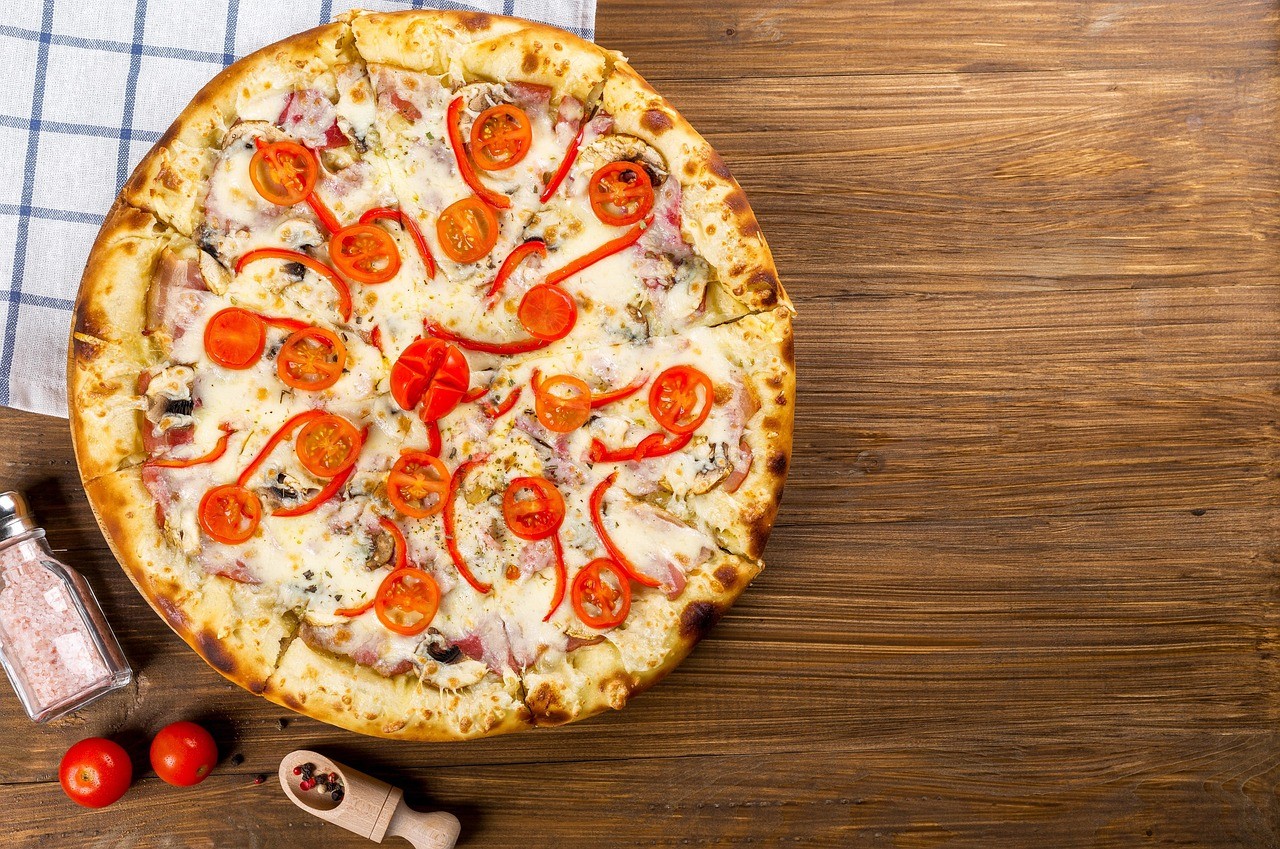 A freshly baked pizza topped with cheese and pepperoni on a wooden surface, with a checkered napkin nearby.