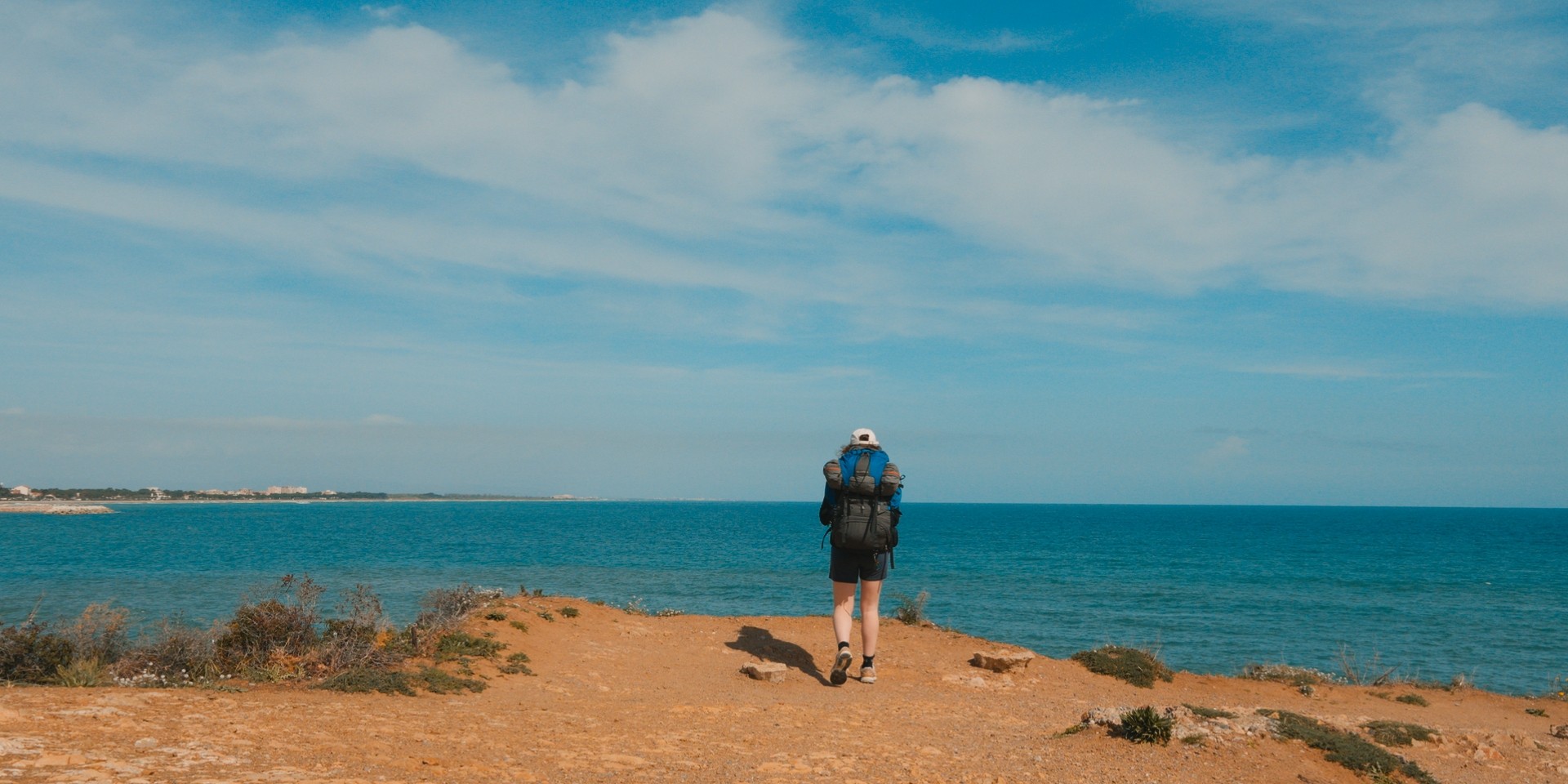 Randonneuse avec sac à dos marchant vers la mer sous un ciel bleu dégagé.