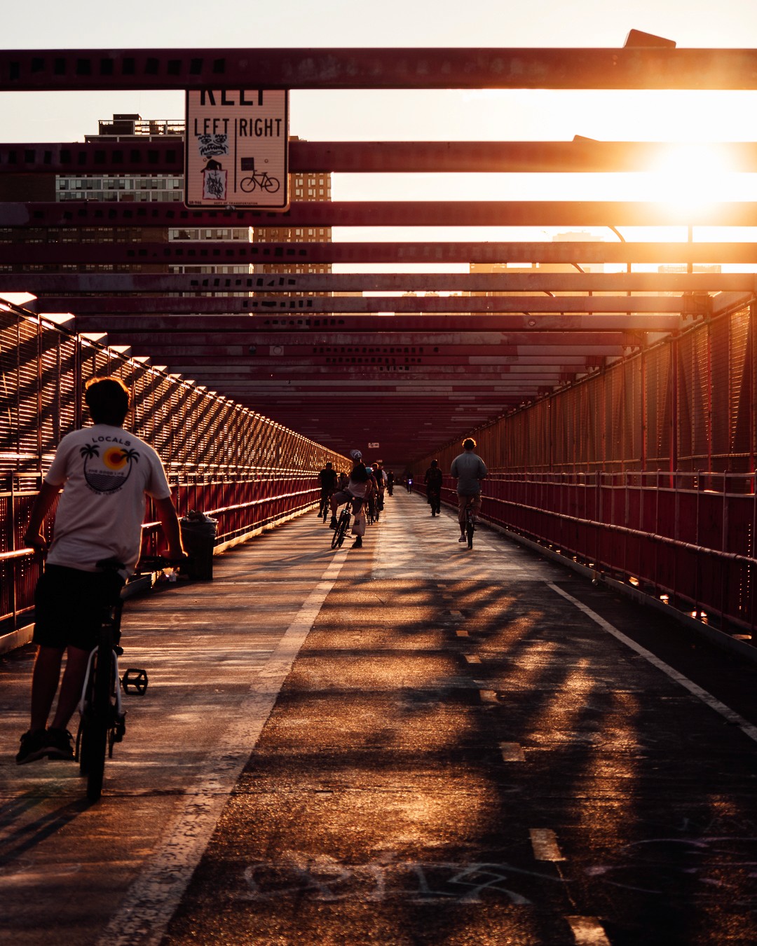 Orange sunset toned photo of williamsburg bridge in nyc with cyclists & pedestrians.