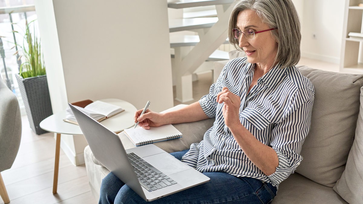 A woman sitting on the sofa and taking notes during a remote design thinking workshop