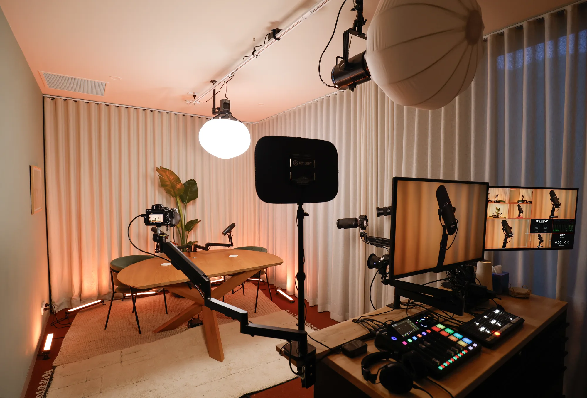 A podcast studio set up with a wooden table, microphones, camera and control desk