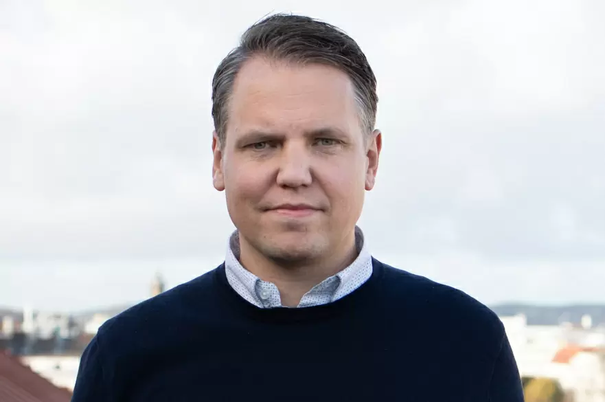 Porträtt av en man med mörkt hår och en mörkblå tröja, ser direkt in i kameran.