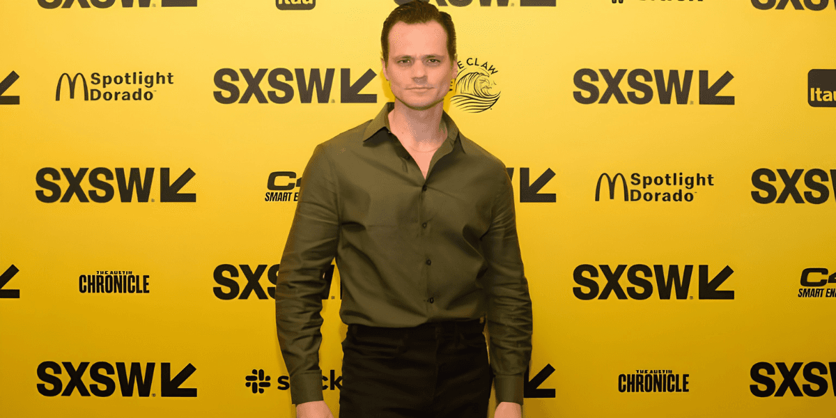 Aaron Dalla Villa poses on the SXSW red carpet in a dark green shirt against a yellow backdrop.
