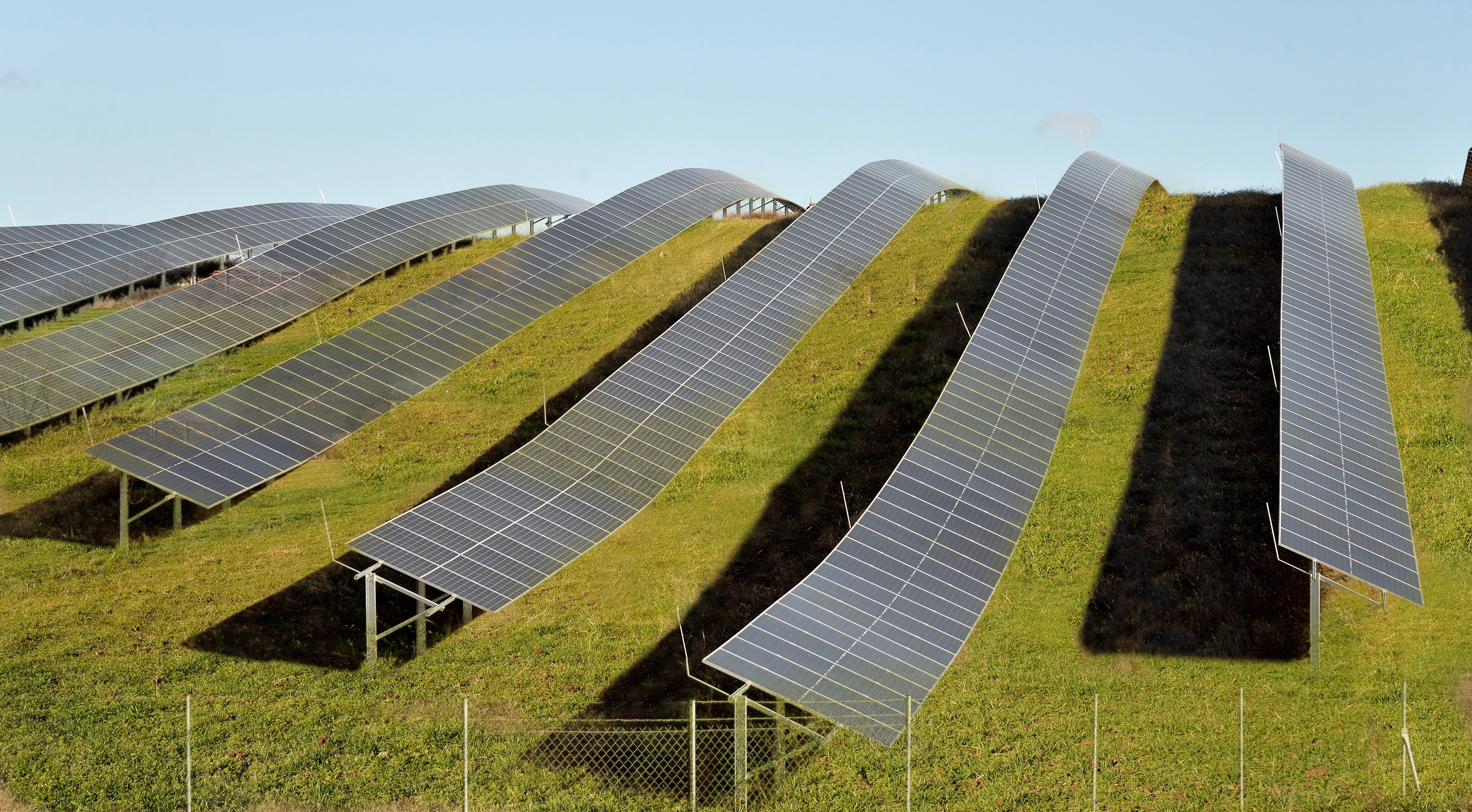 Ground-mounted photovoltaic panels arranged in curved rows across sloped green terrain