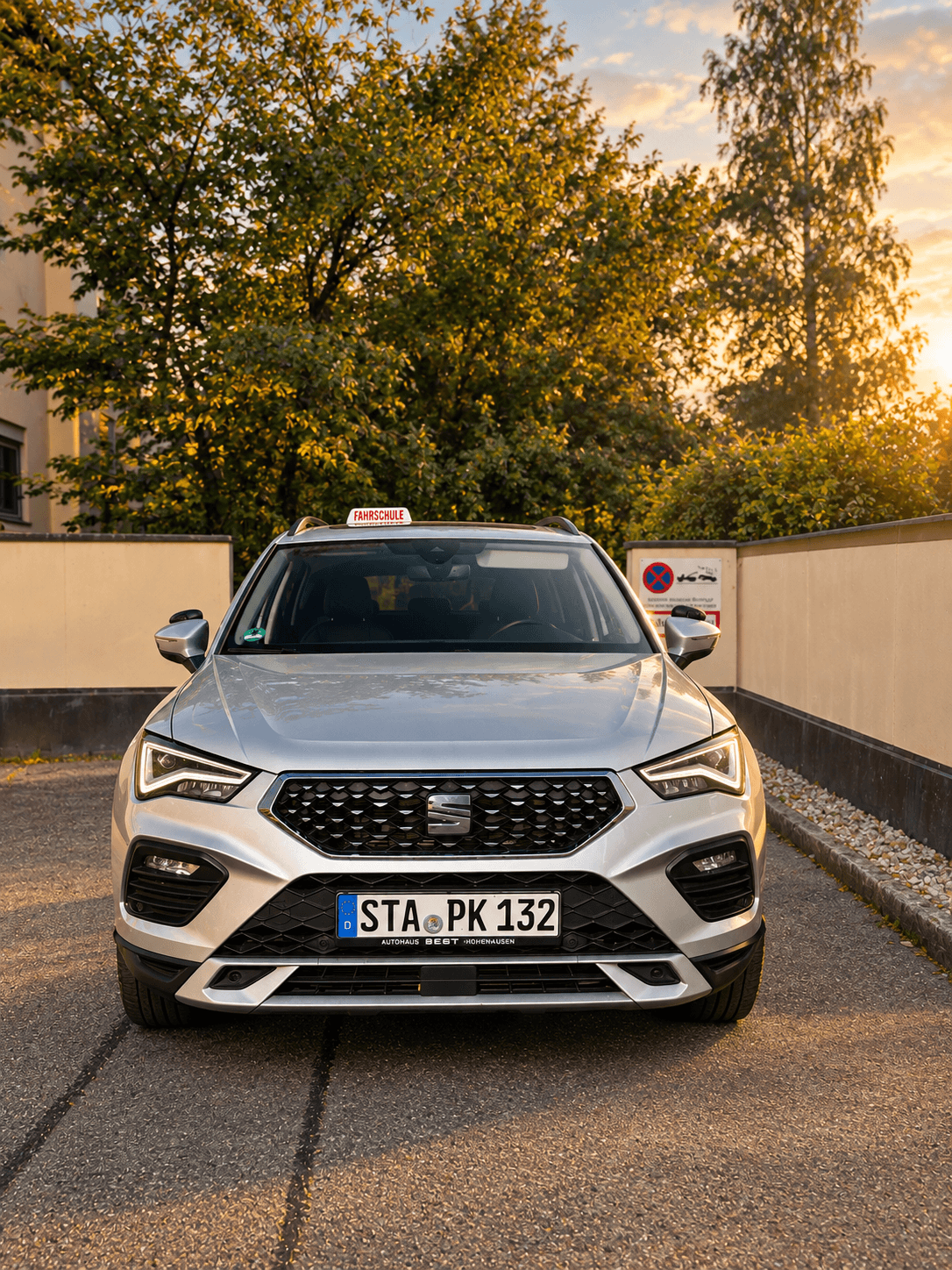 Ein weißer BMW 2er Gran Tourer als Fahrschulwagen mit dem Kennzeichen STA-PK 129 parkt in der Einfahrt vor einem gelben Gebäude.