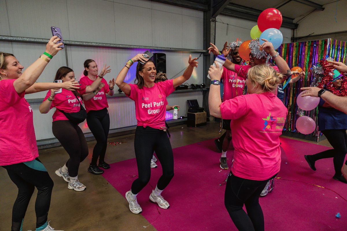 Outdoor team-building event with participants wearing matching blue shirts, taking part in inflatable obstacle courses and games, smiling and cheering, with the words 'ENTER A TEAM' in large bold white and green text across the image.
