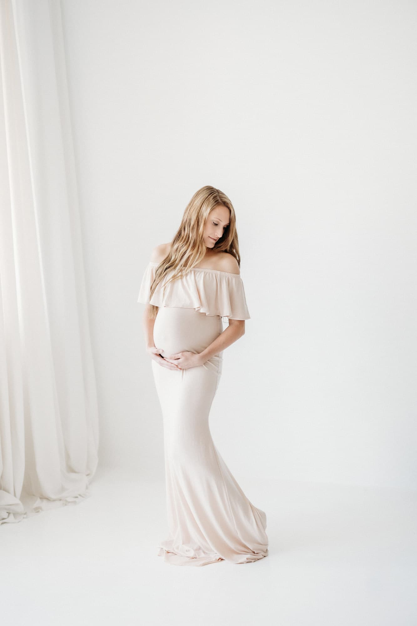 A pregnant mother and her daughter hold hands and smile in a bright, natural light setting at Revelator Studio in Shreveport, featuring maternity photography.