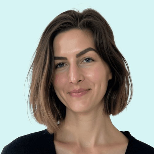 A person with wavy light hair stands facing slightly to the left, wearing a striped shirt against a neutral background.