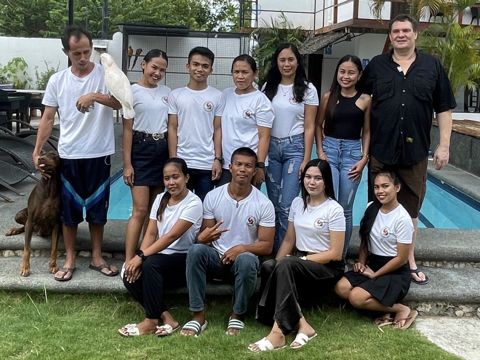 Group of staff and guests posing by a pool with a parrot.