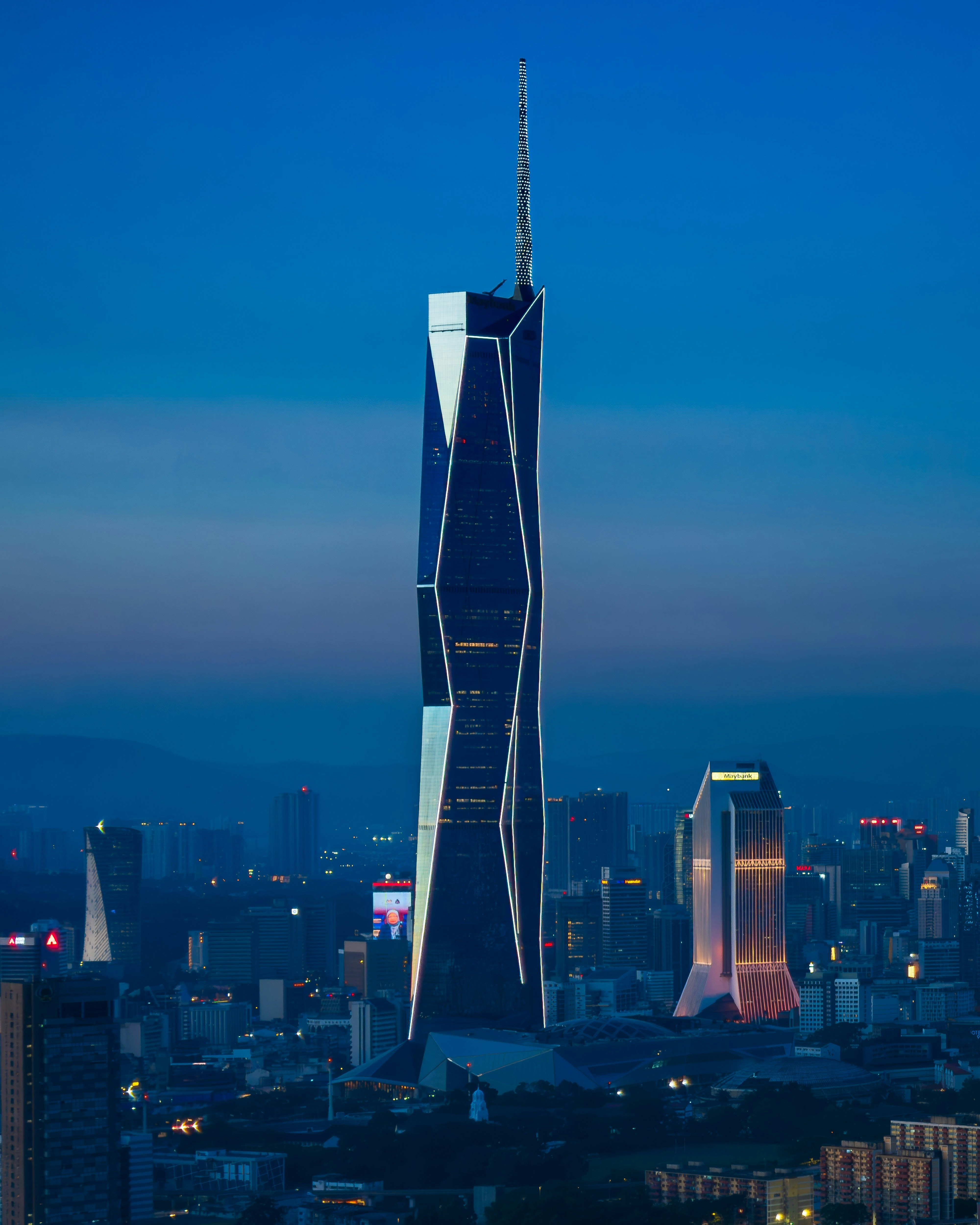 Modern skyscraper illuminated at dusk with city skyline.