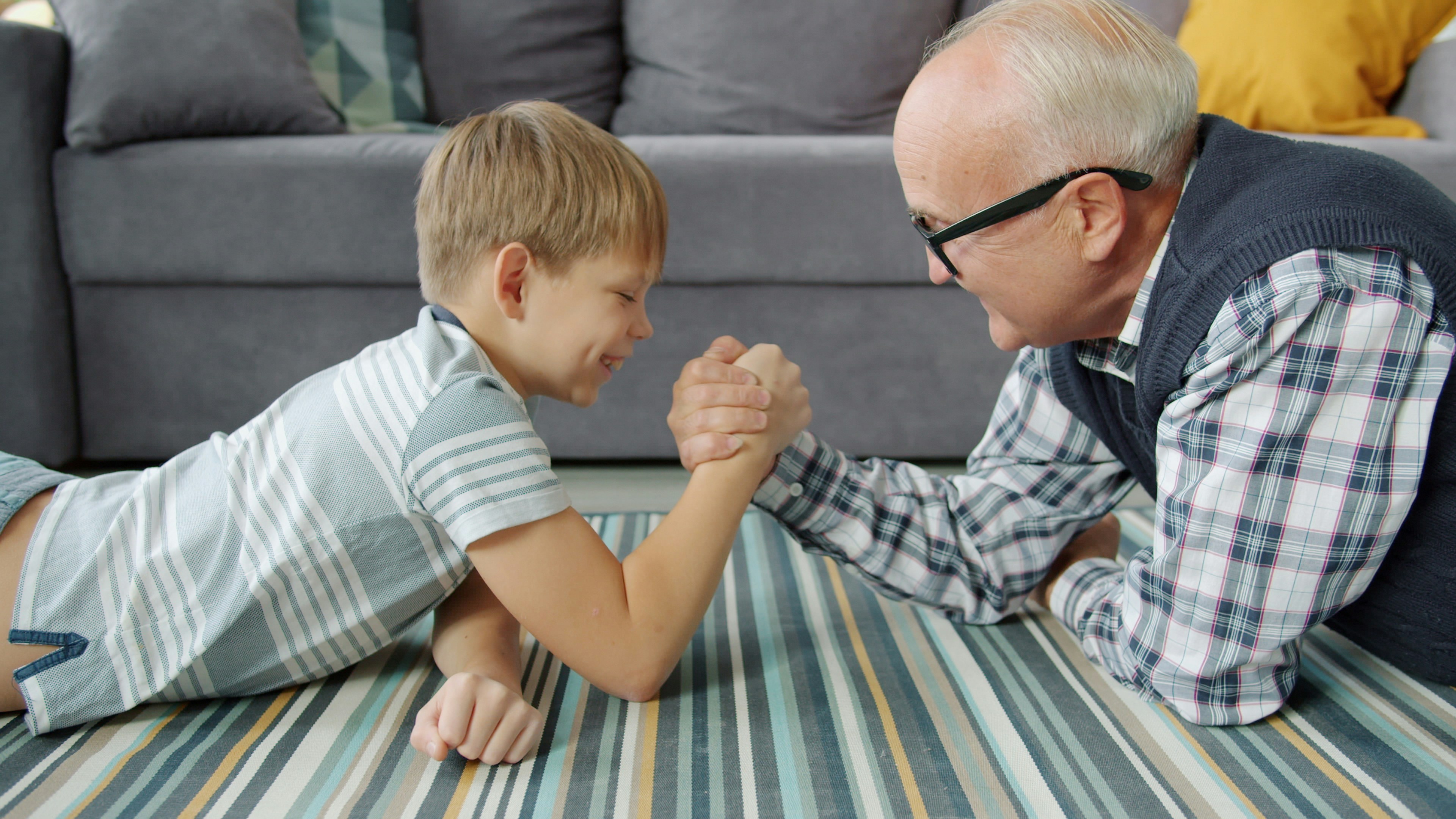 Grandfather and grandson arm wrestling on the floor