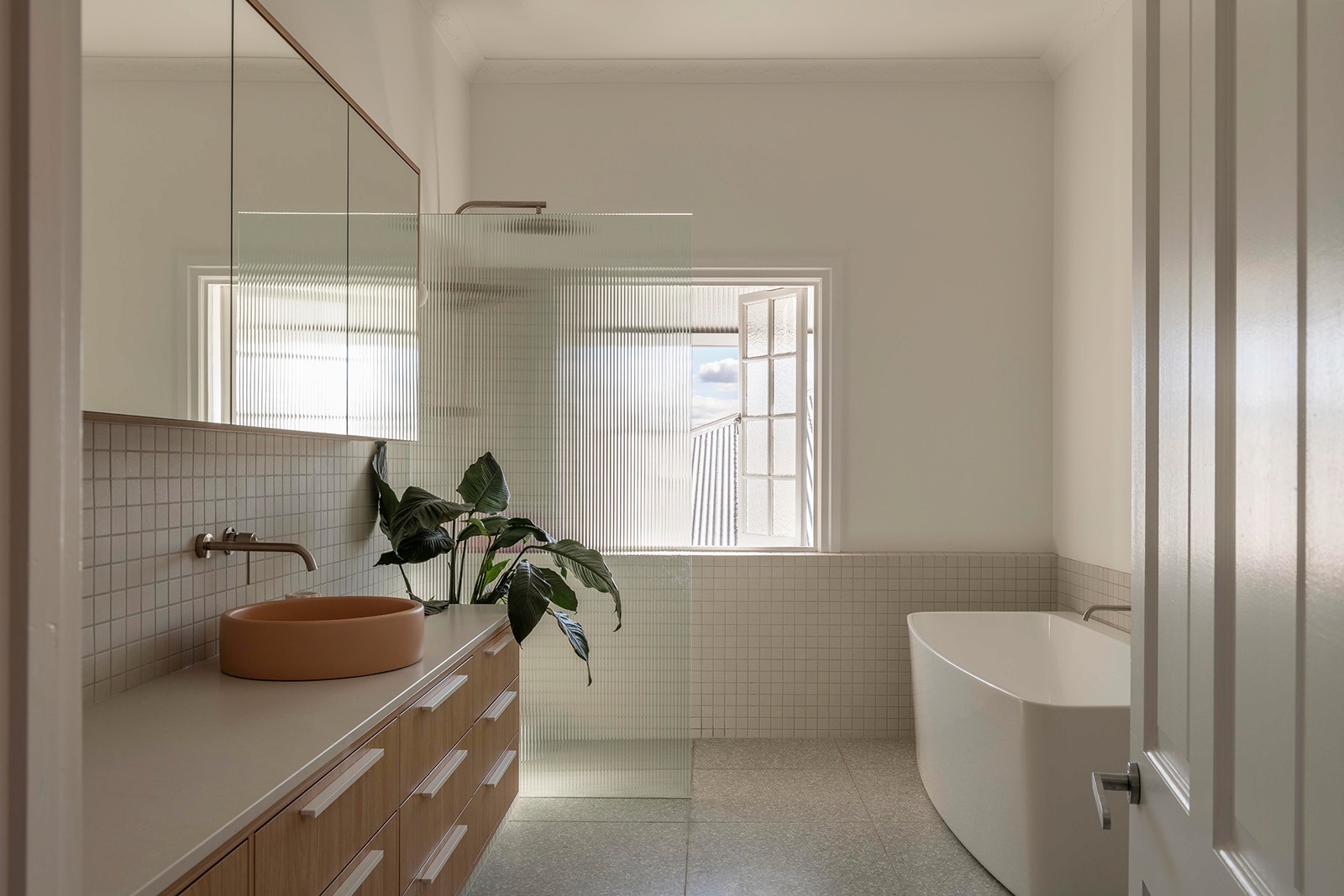Light-filled bathroom with freestanding tub, terrazzo floor, timber vanity, and frosted window for privacy.