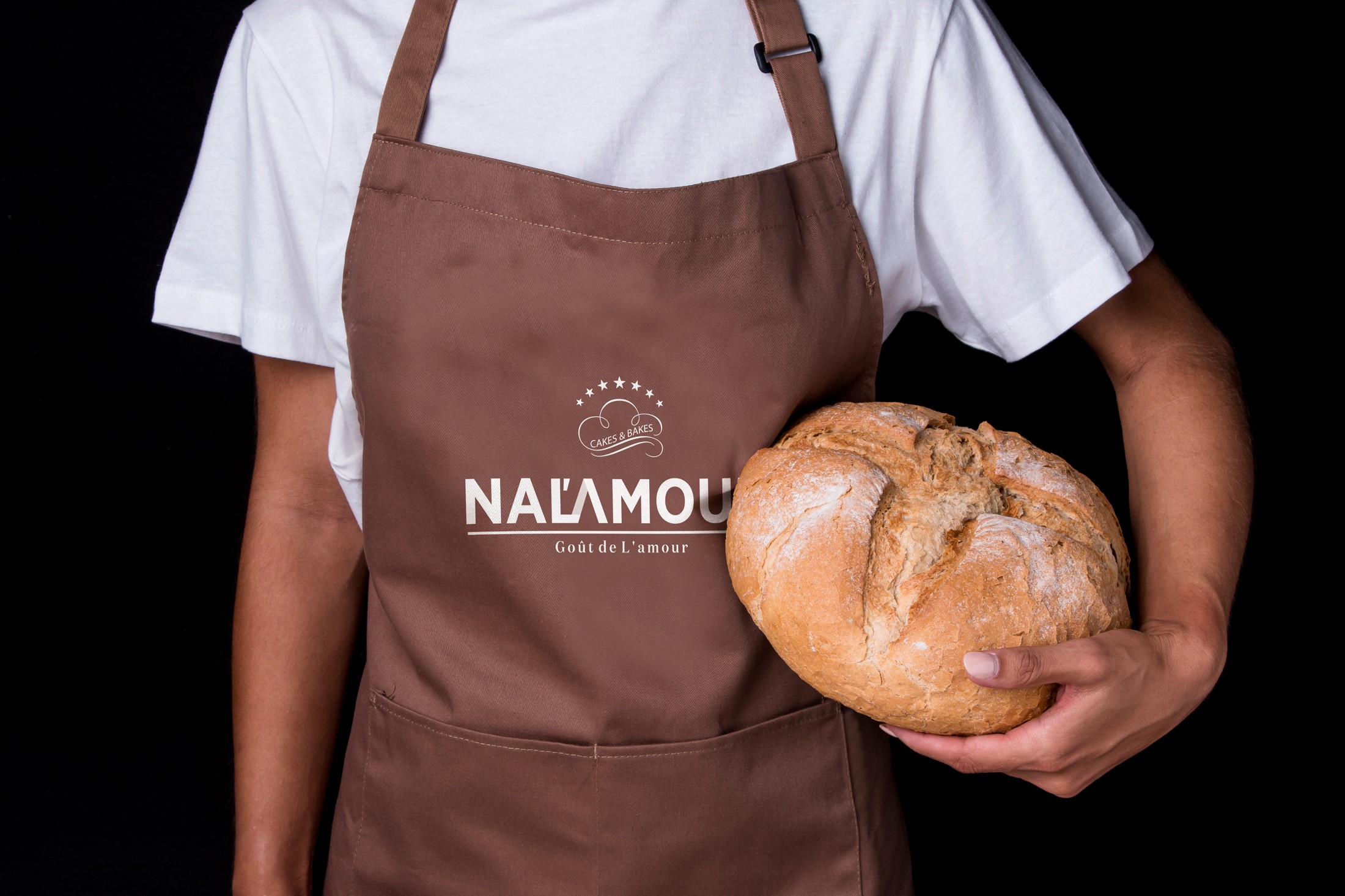 Home baker standing with bread in hand wearing apron with brand logo nalamour