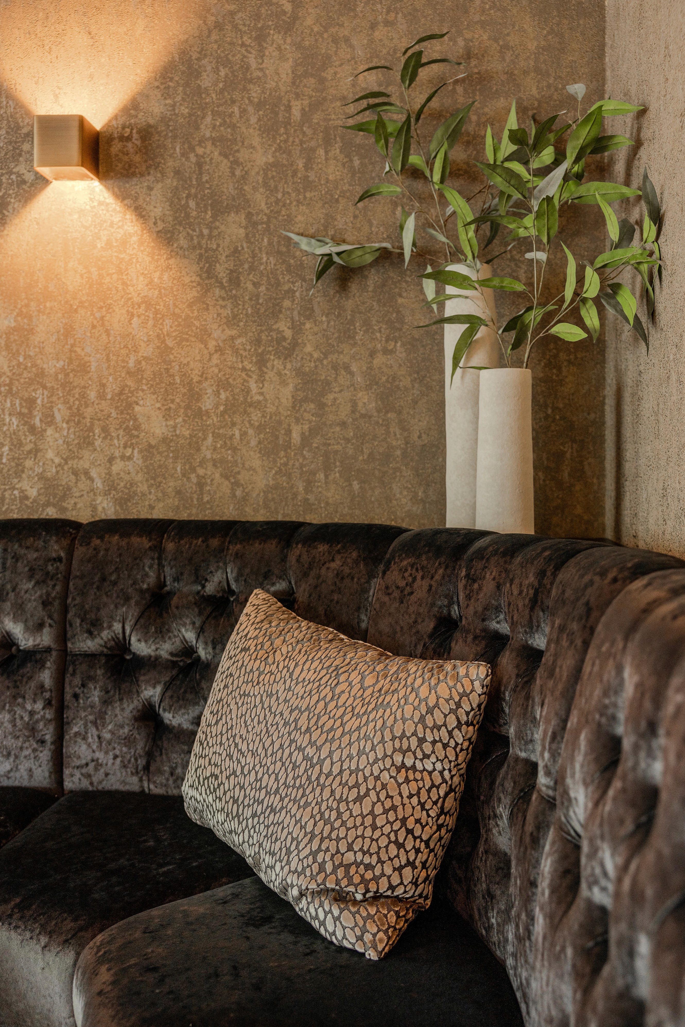 Sfeerhoek in het interieur van Destin: donker fluwelen zithoek met slangenprint sierkussen, witte vaas met takken en dimbare wandverlichting – DSN Workspace Solutions