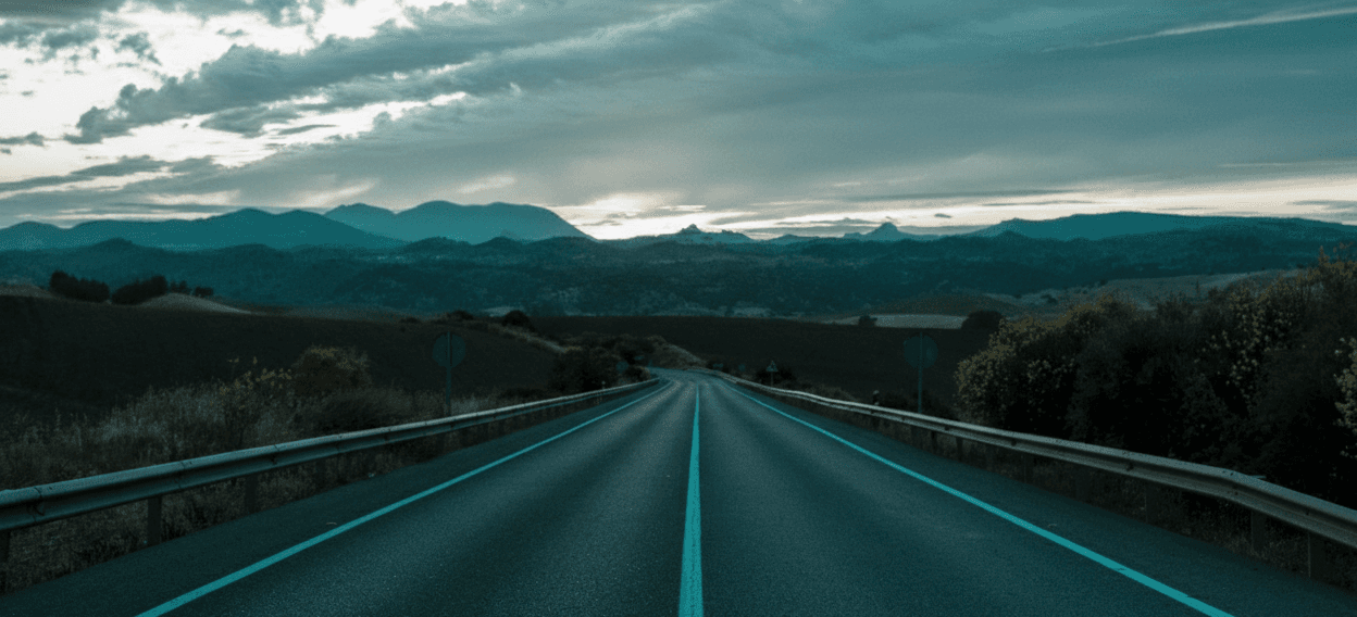 a long empty road with a yellow field in the background