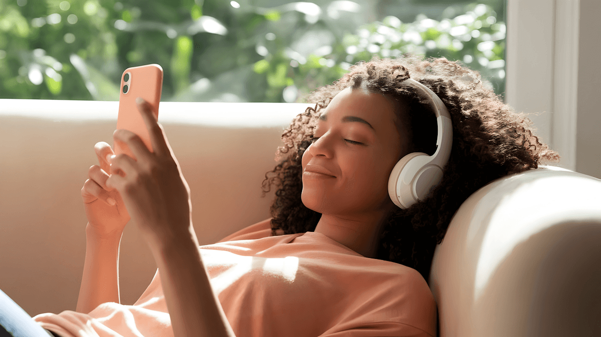Woman with curly hair relaxing on couch with headphones and phone