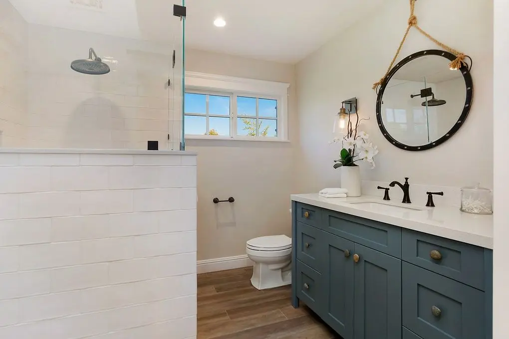 'Port Streets Remodel' bathroom with a walk-in shower, round mirror, nautical accents, and a teal vanity.