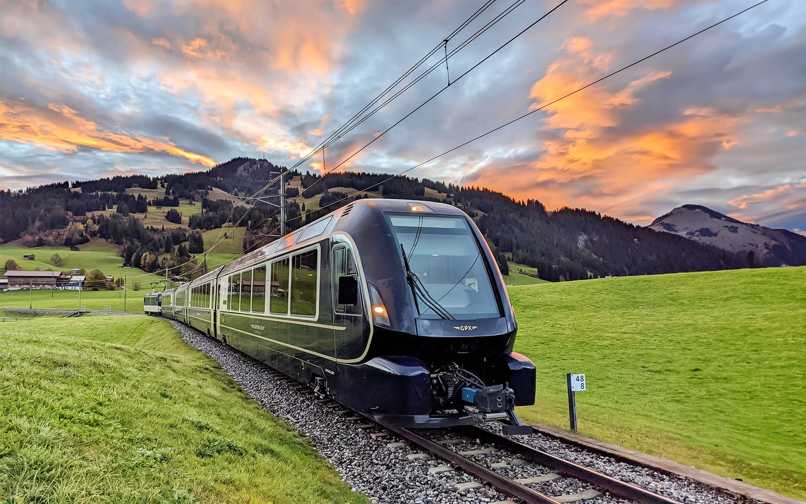 GoldenPass Express train traveling through scenic Swiss countryside near Interlaken at sunset.