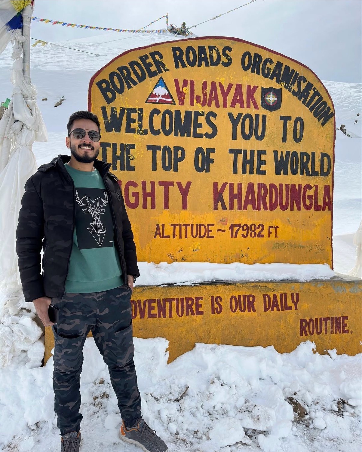 A view from an airplane window shows the aircraft's wing with a golden hue reflecting the setting sun, against a serene backdrop of fluffy clouds and a clear sky.