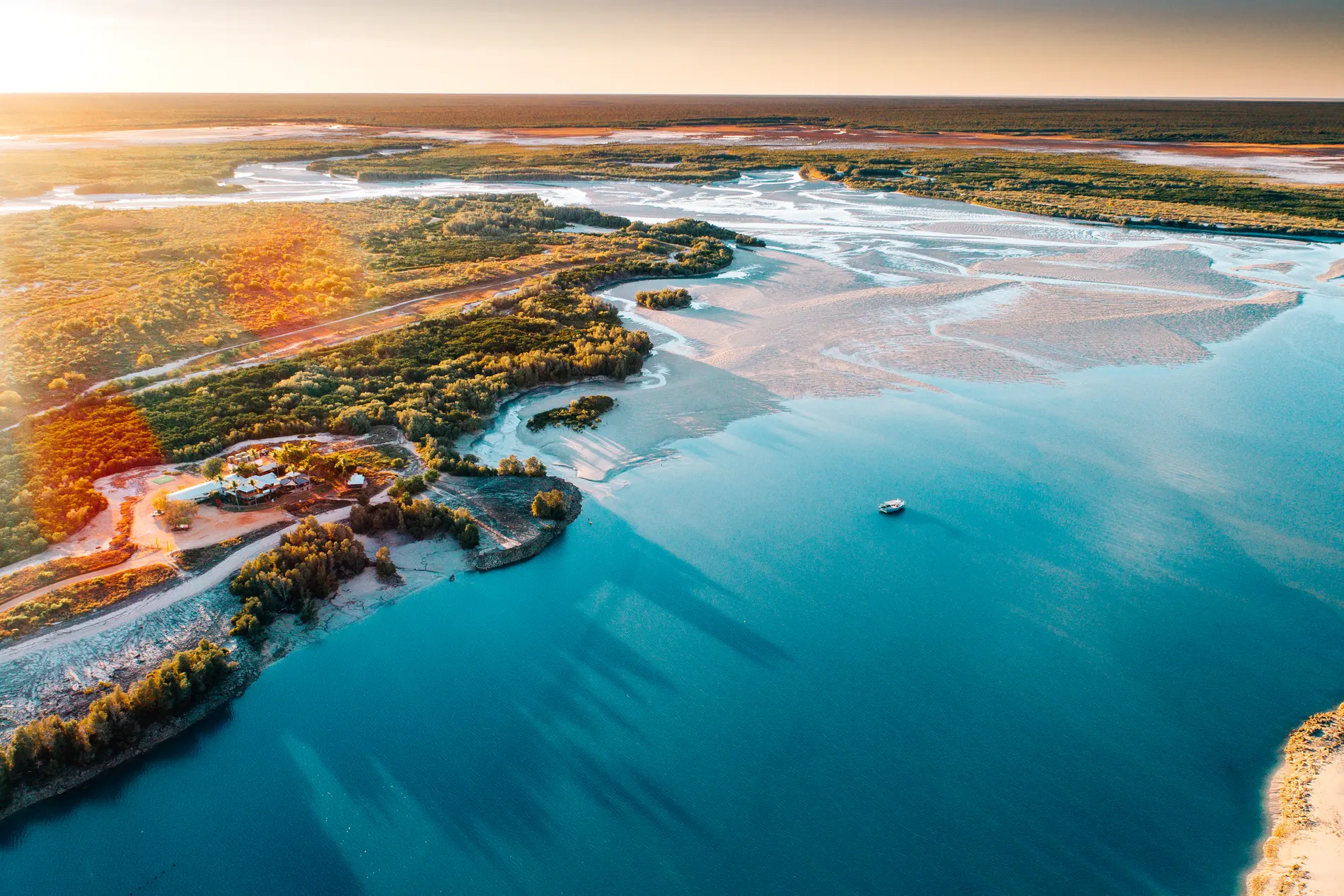 Aerial at sunrise over a tidal estuary, a single boat anchored among the sandbanks