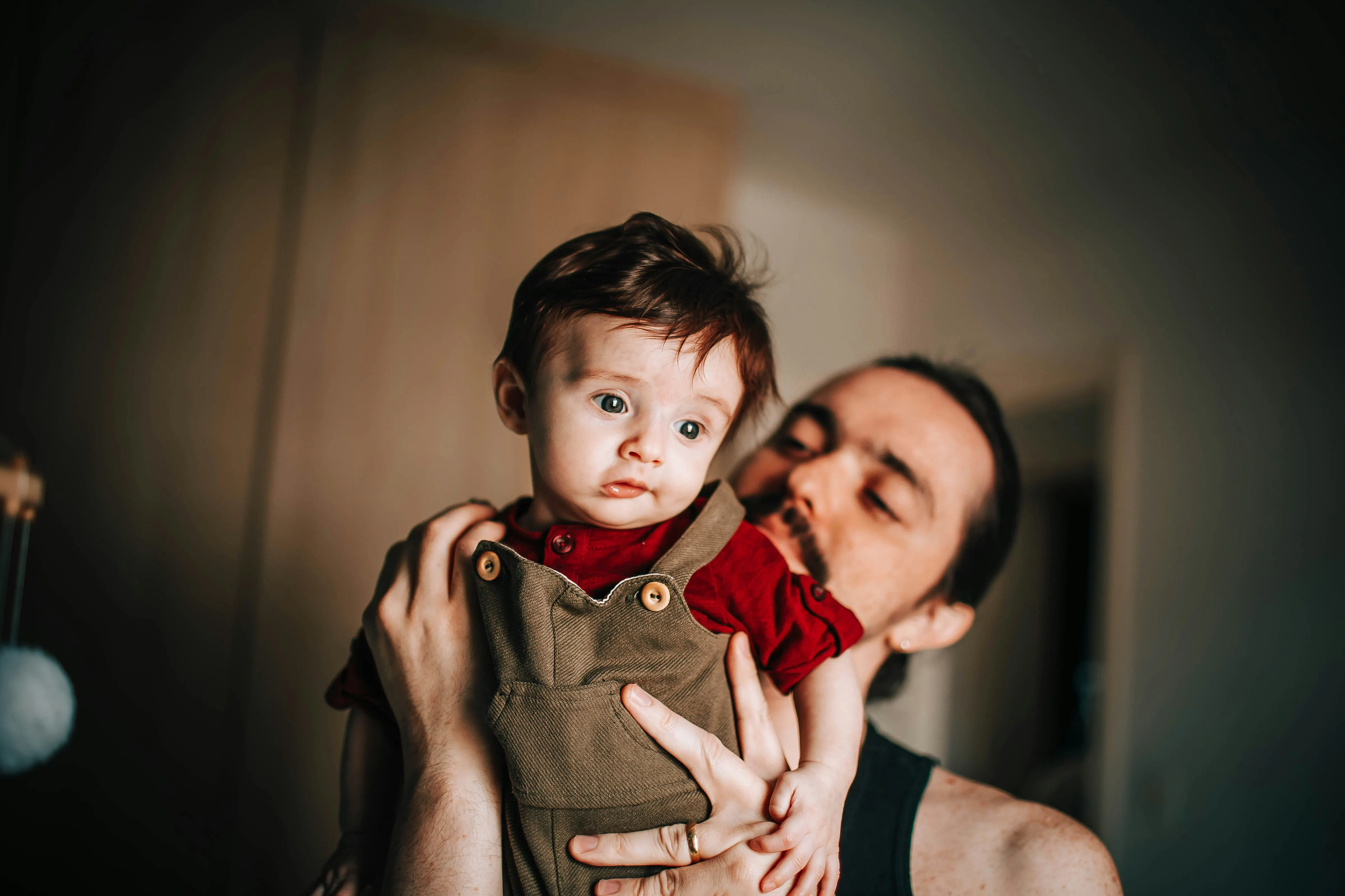 father holding a baby boy. the baby is wearing a brown overall and red shirt