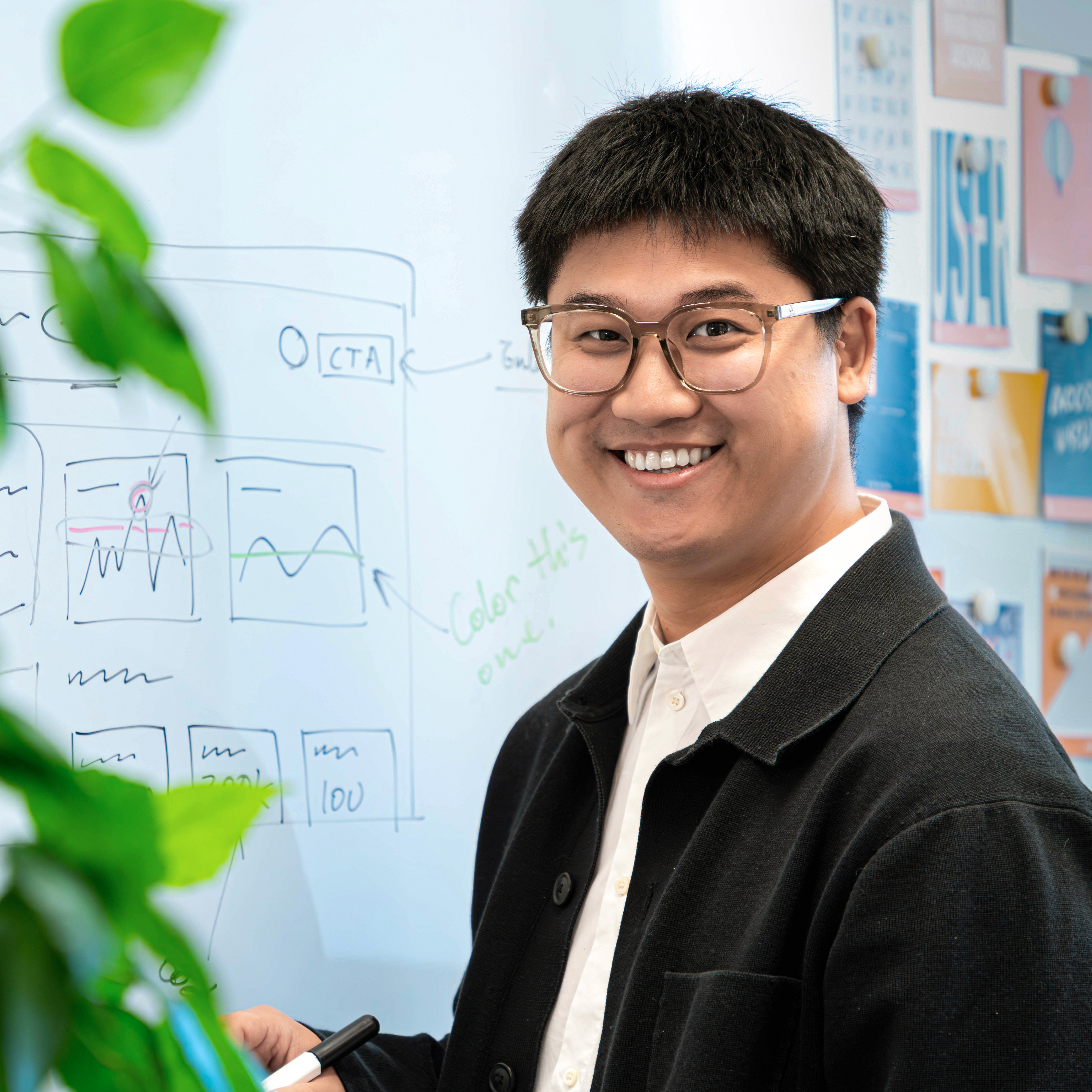 Person in schwarzer Jacke und weißem Hemd steht vor einem Whiteboard mit Diagrammen und Texten