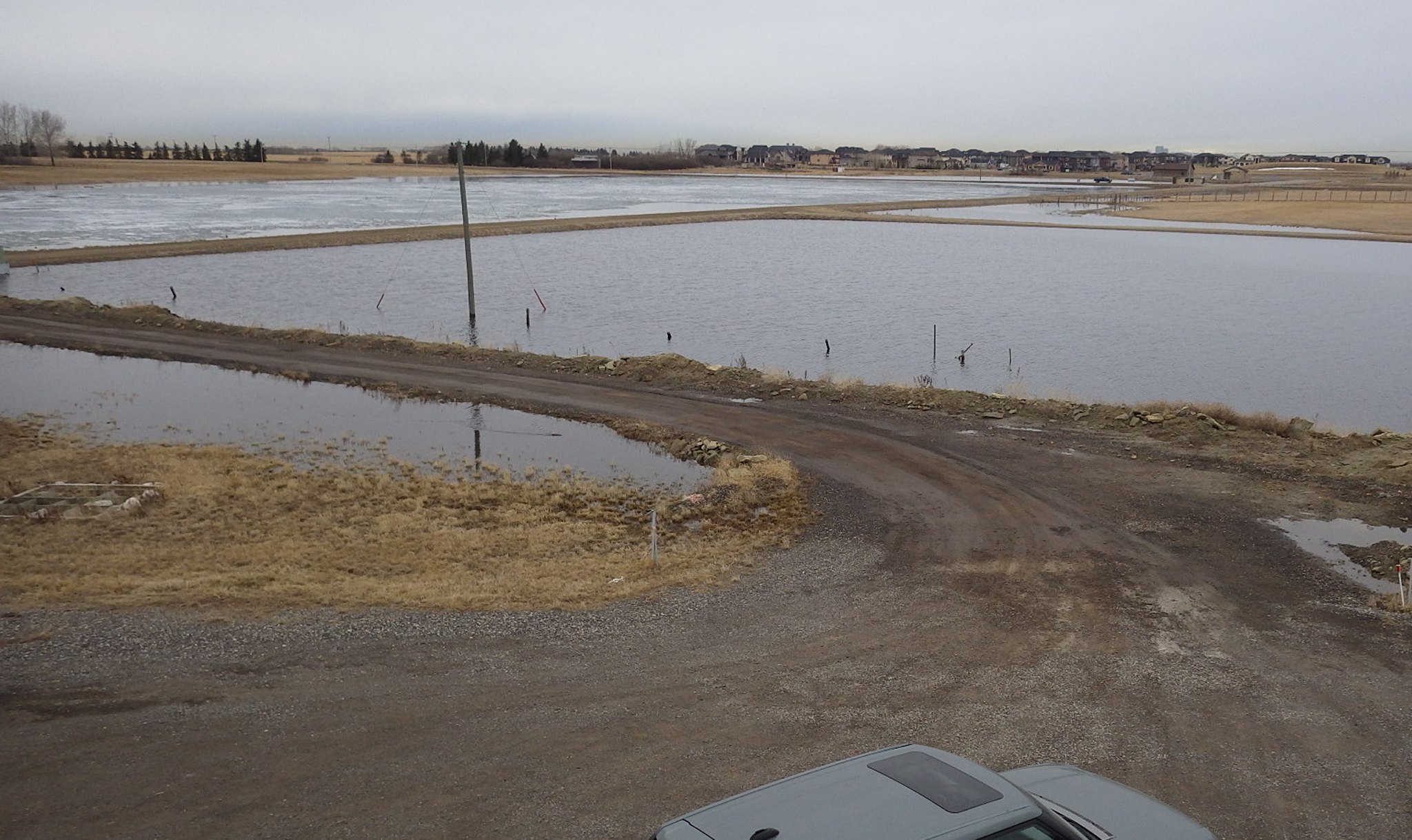 Flooded rural access road and agricultural land near residential development