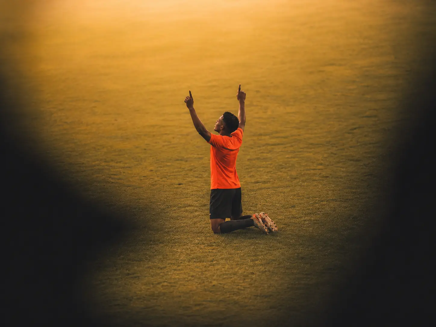 Football player kneeling on the pitch celebrating a goal with arms raised