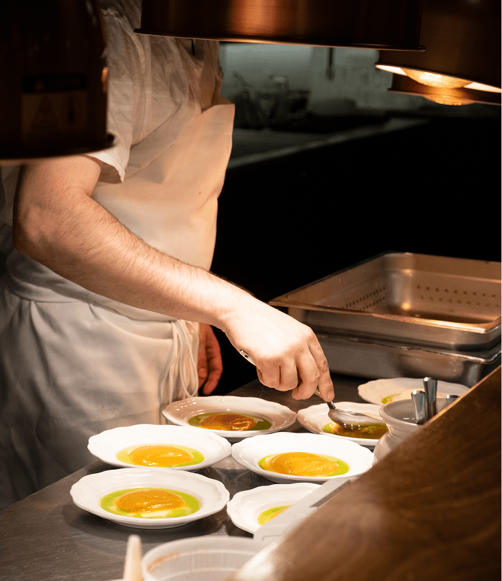 Un cuisinier prépare les accompagnements de purée de courge et oeuf mollet.