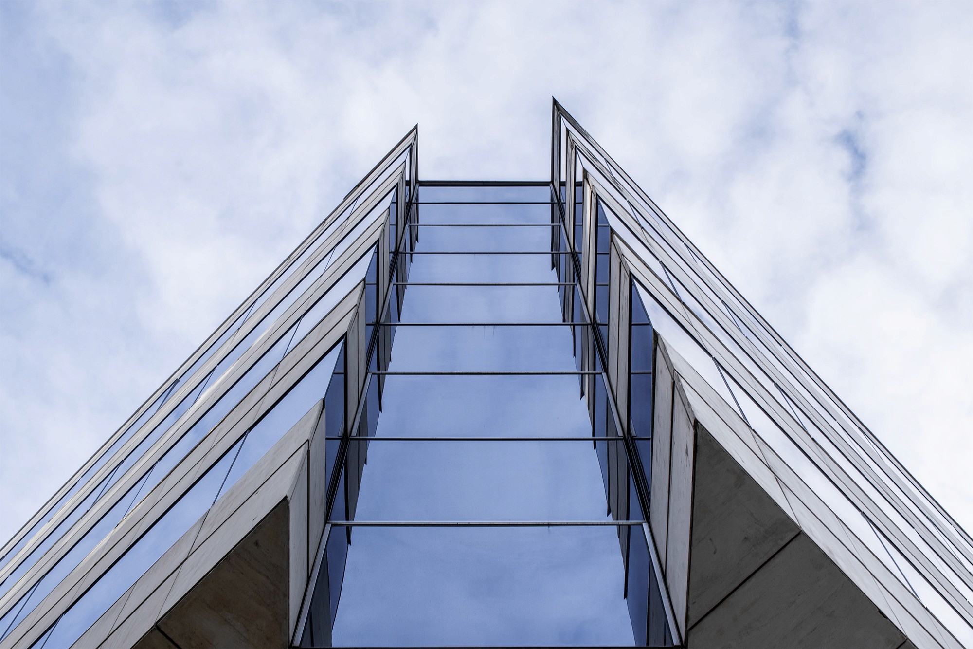 Upward view of a modern glass building against a cloudy sky